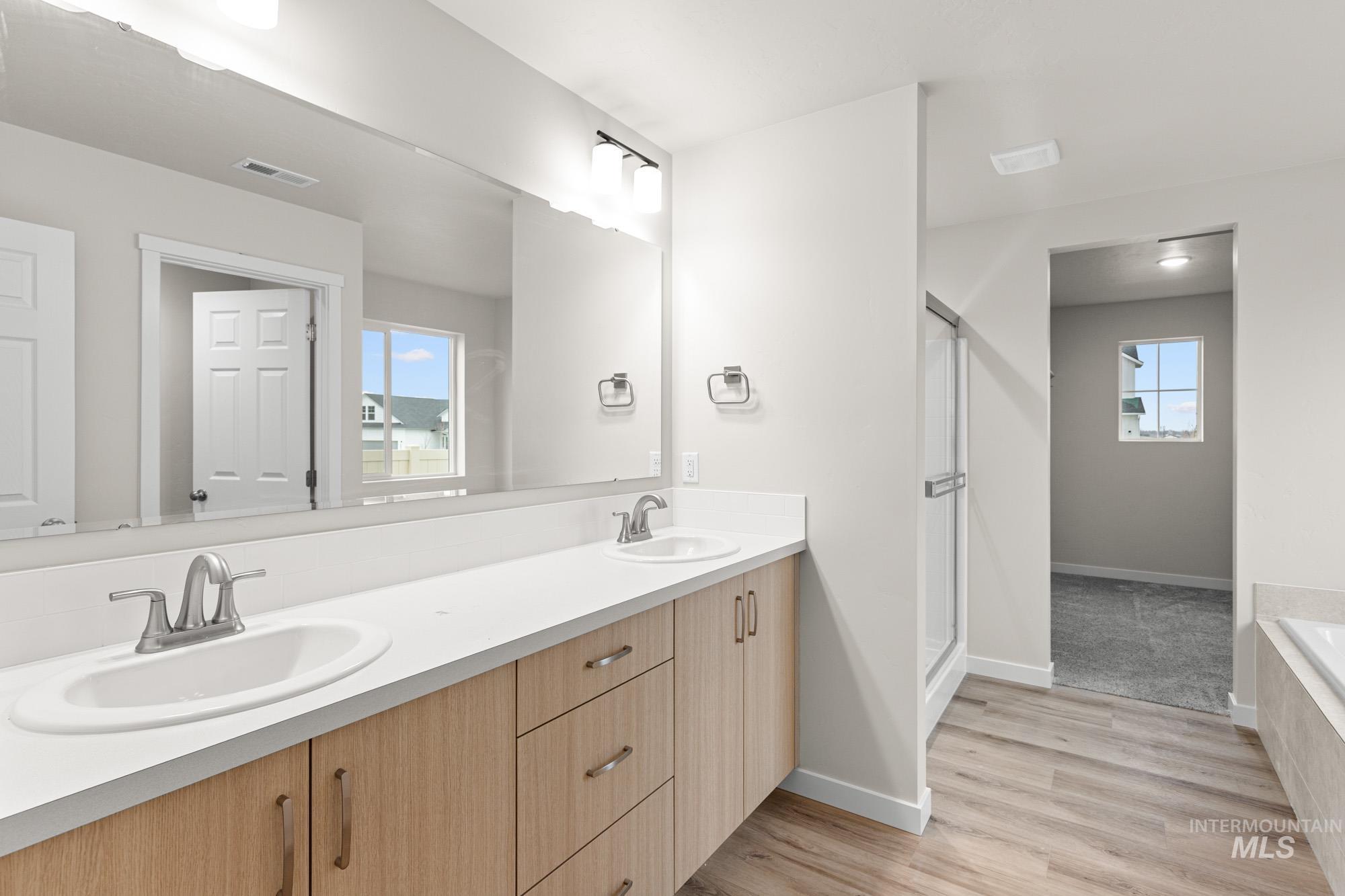 Bathroom featuring double vanity, light wood-style flooring, a stall shower, and tiled tub