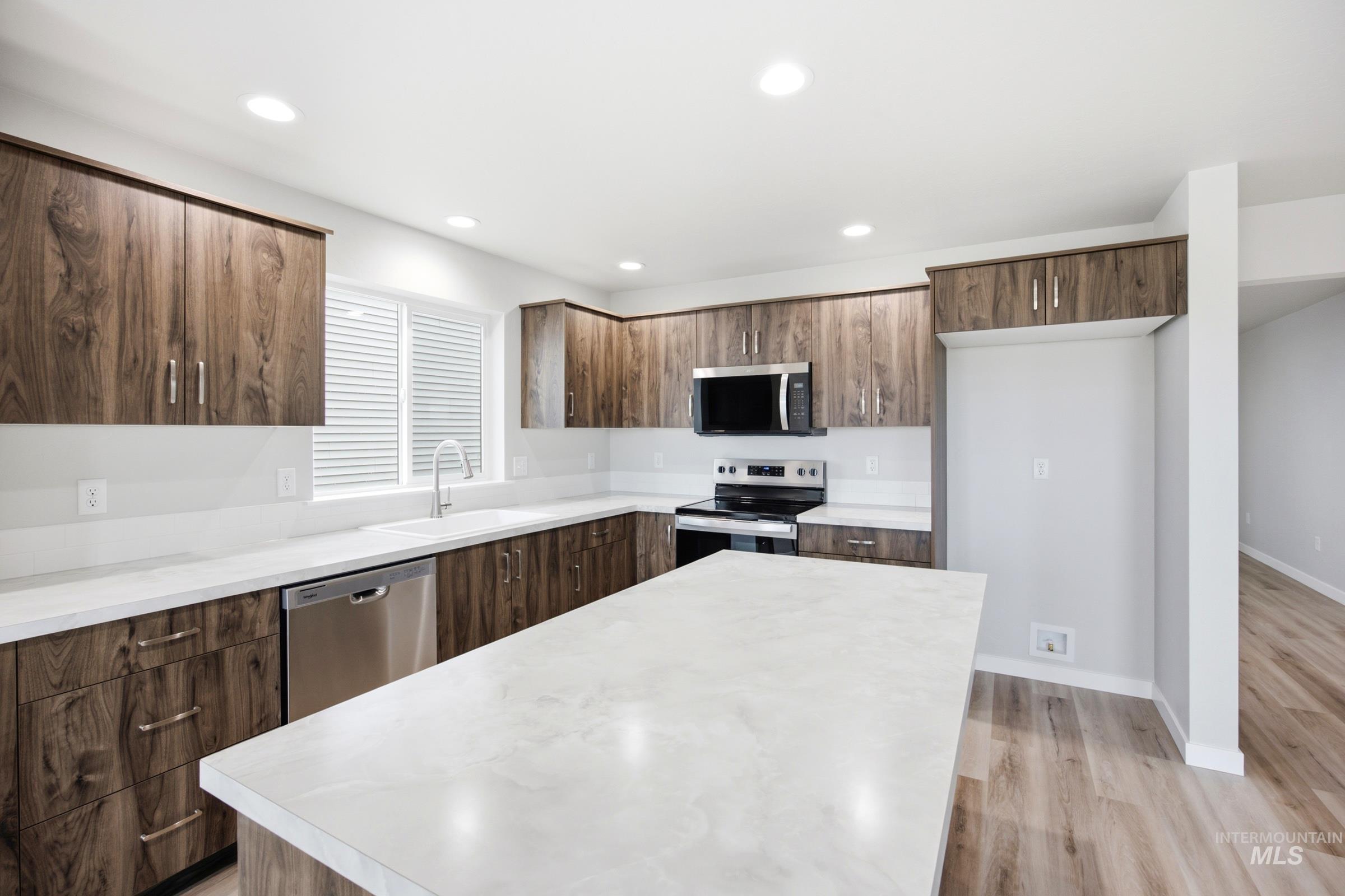 Contemporary kitchen featuring wood-finish cabinetry, light-toned countertops, and stainless steel appliances