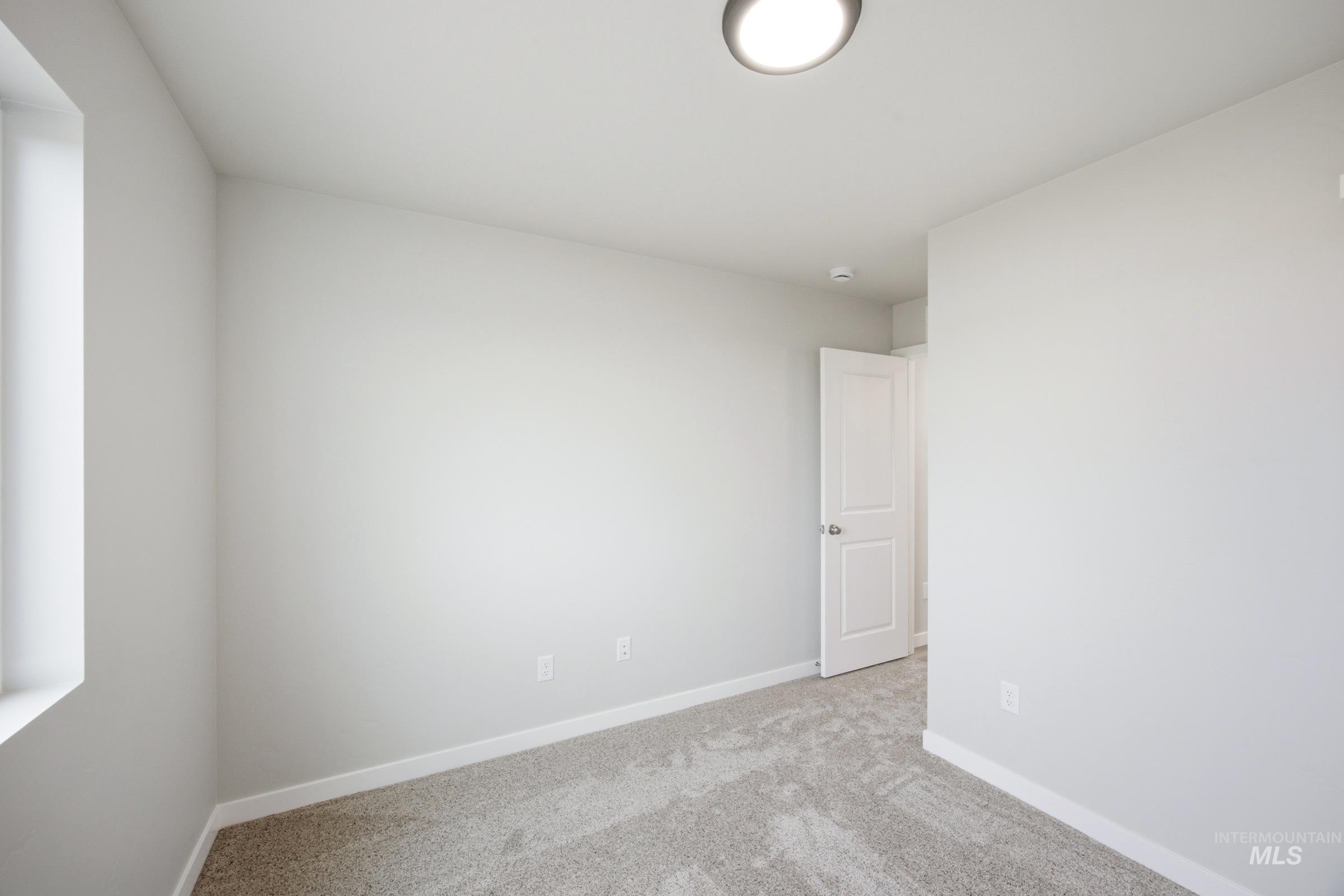 Neutral gray wall finishes, light gray carpet, white trim, recessed window, and a white interior door with a chrome handle