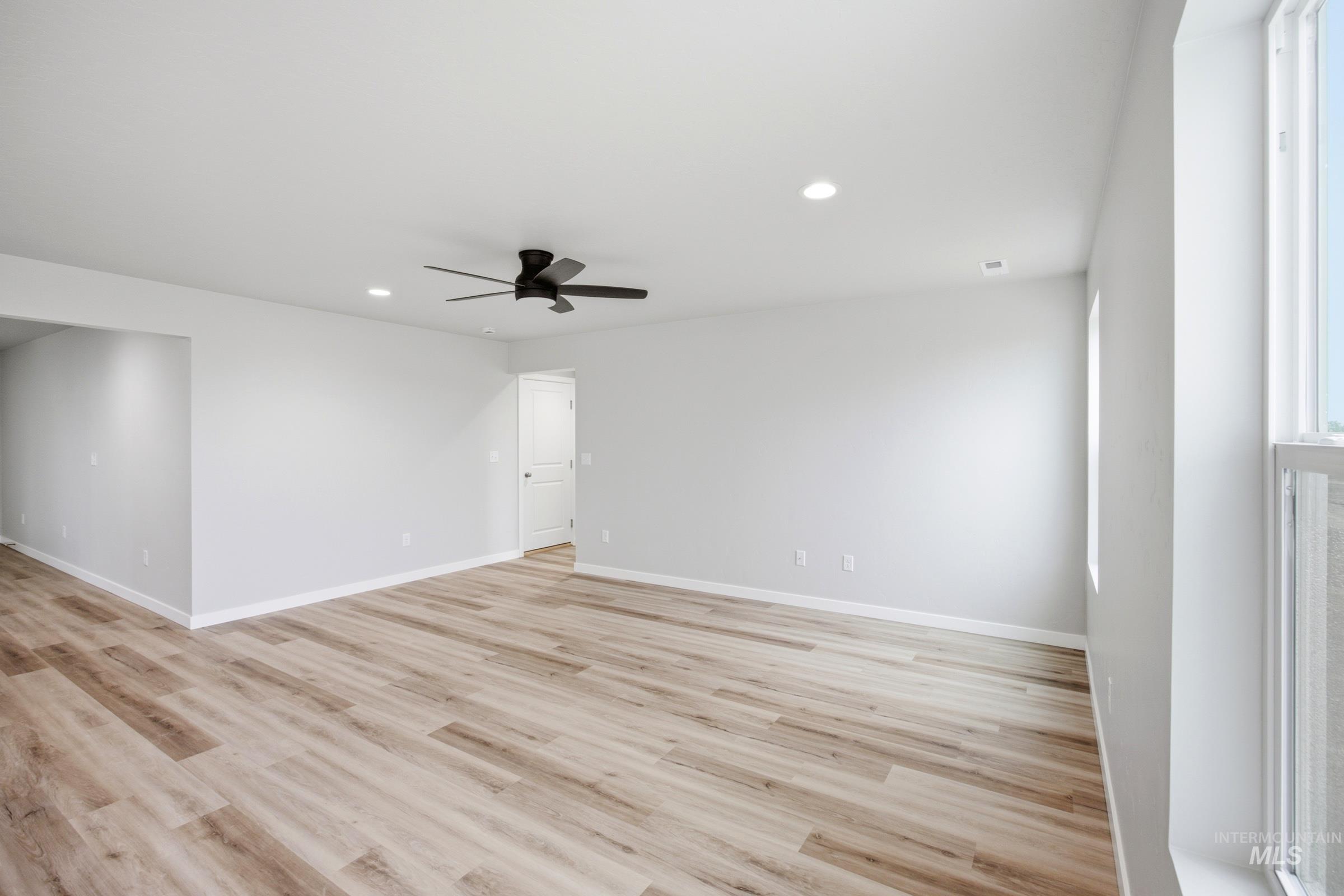 Spacious room featuring wood-finish flooring, light gray walls, white trim, and a black ceiling fan with integrated lighting