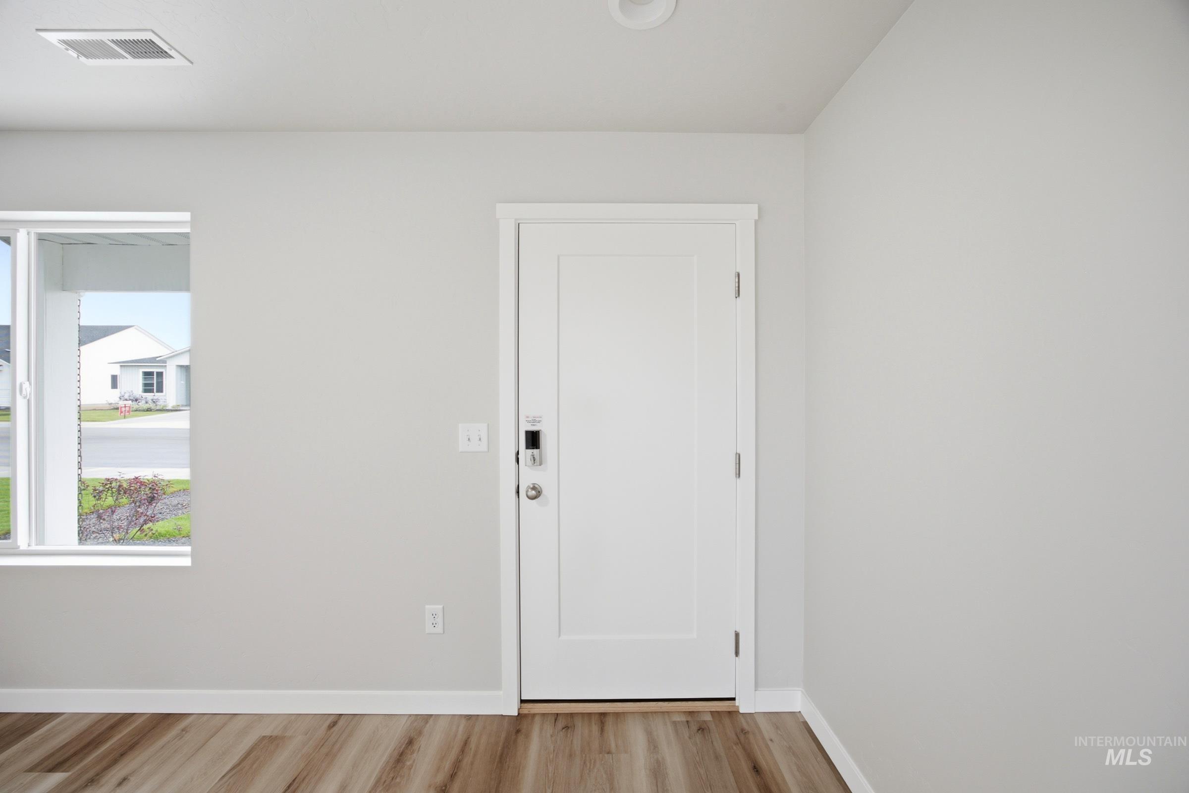 Entryway featuring a white paneled door with smart lock hardware, wood-finish flooring, a window with white trim, white baseboards, and light gray walls