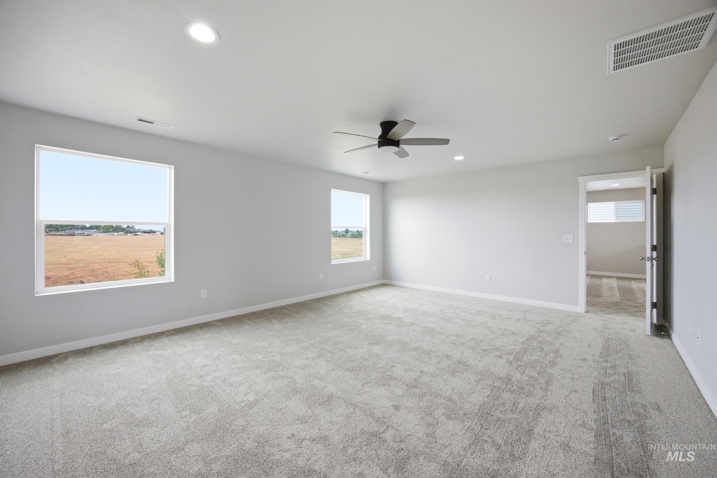 Spacious room featuring light gray walls, plush gray patterned carpeting, a ceiling fan with integrated lighting, and recessed ceiling lights