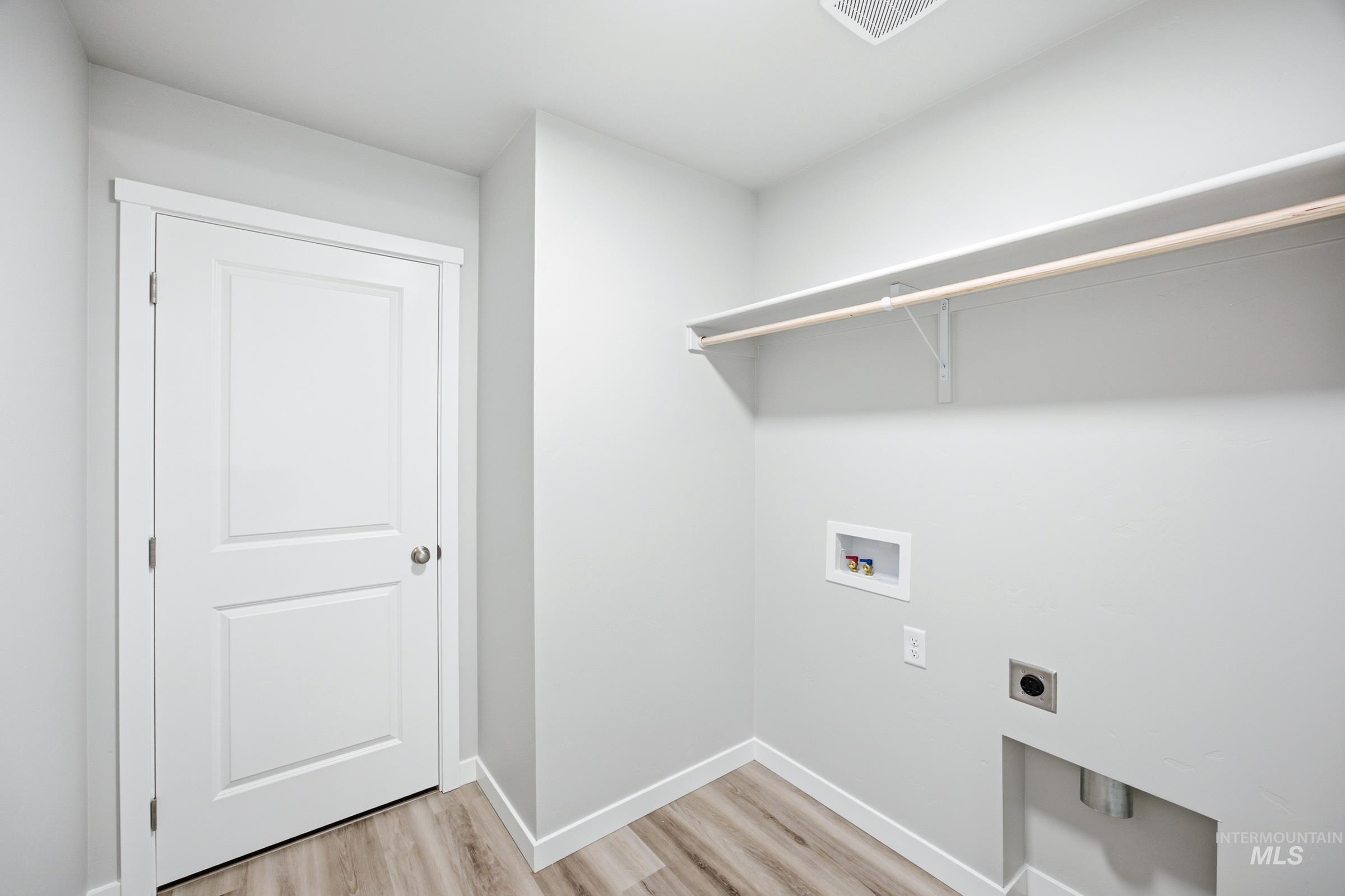 Dedicated laundry area featuring wood-finish flooring, a white two-panel door, built-in shelving, and utility hookups