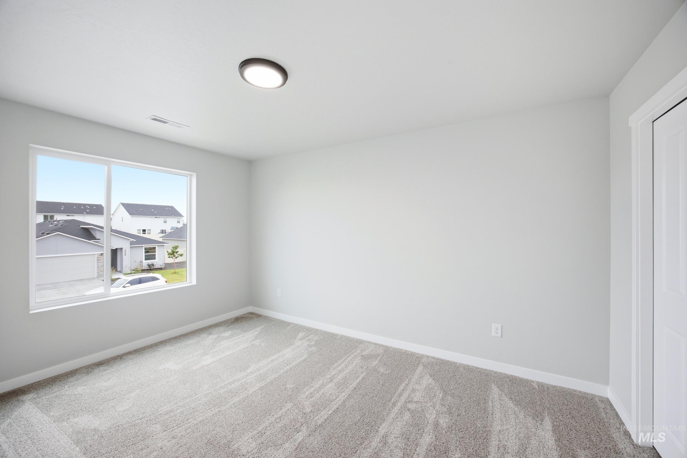 Spacious room featuring neutral wall tones, textured carpet, a large picture window, and a flush-mount ceiling light fixture