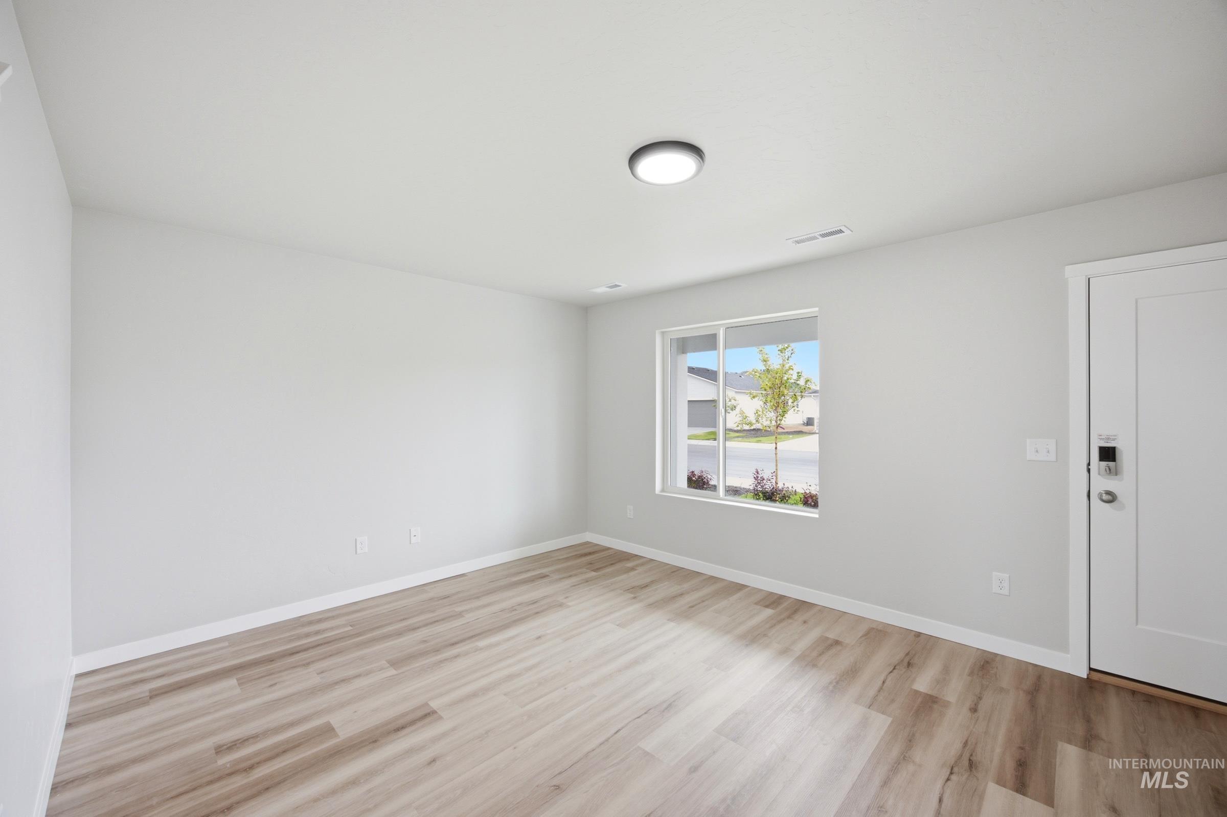 Bright interior space featuring light-toned walls, wood-finish flooring, and a large window with a streetscape beyond