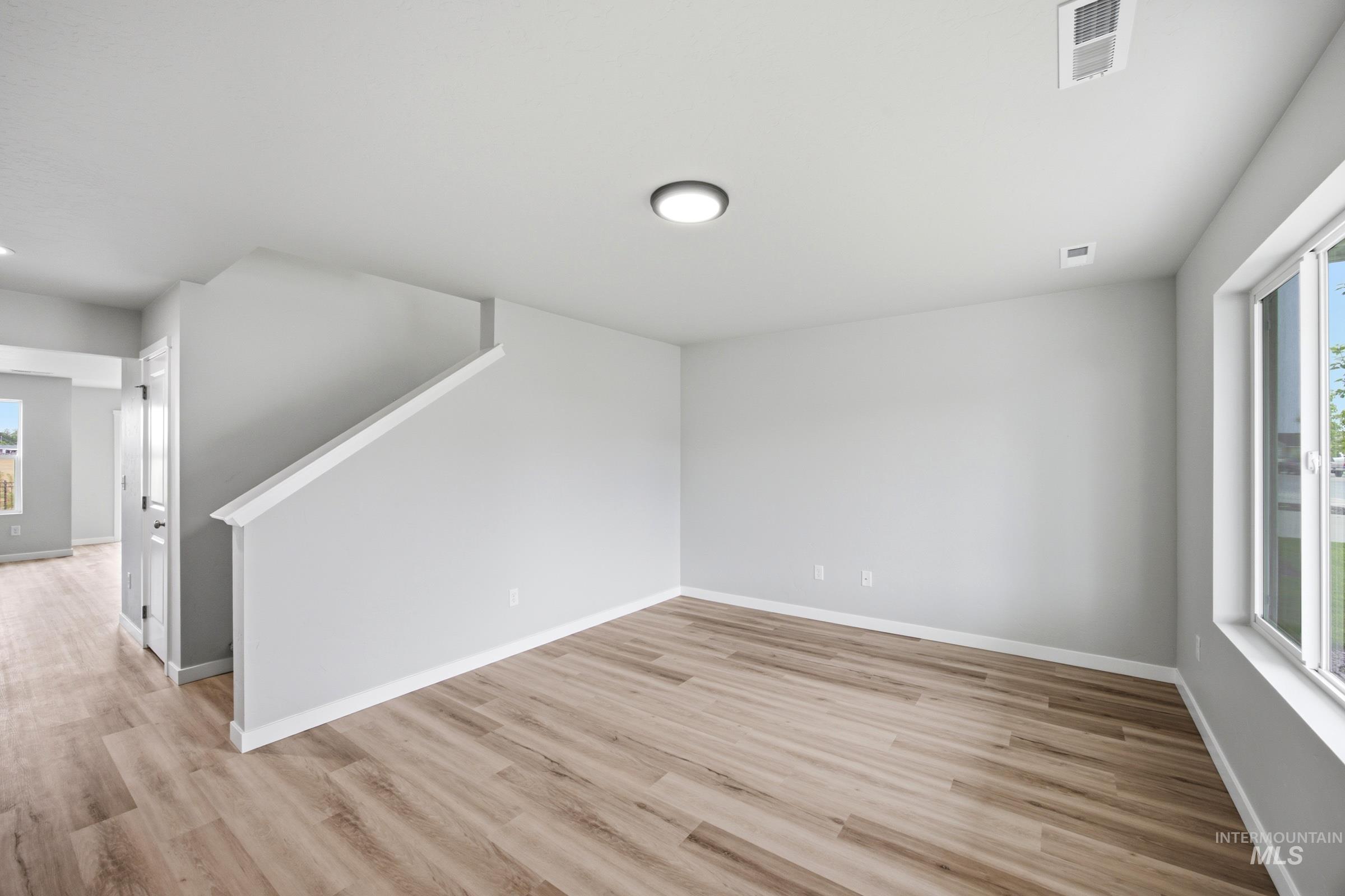 Spacious room featuring wood-finish flooring, light grey walls, white trim, and a contemporary ceiling light fixture