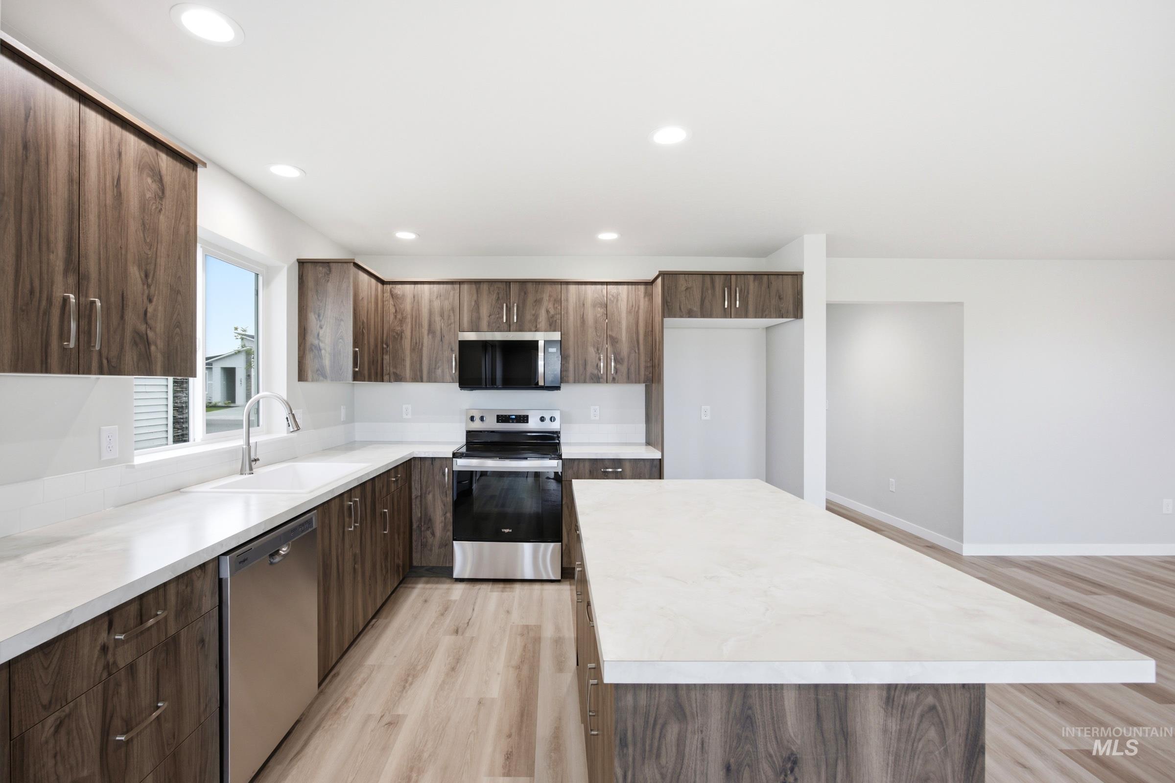 Modern kitchen featuring wood-finish cabinetry, white countertops, and stainless steel appliances