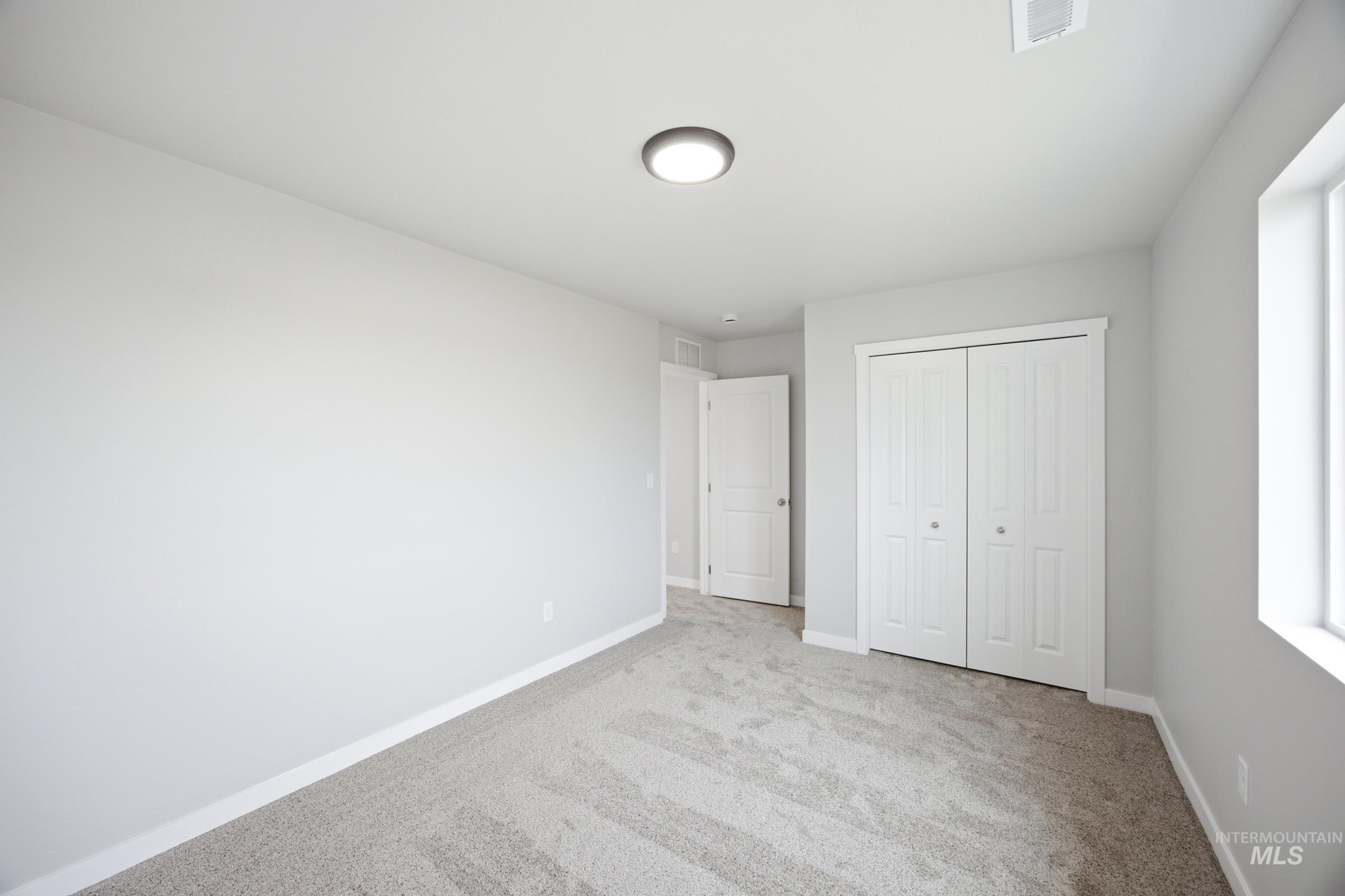 Carpeted room with light gray walls, a flush-mount ceiling light, a white bi-fold closet, and a single window providing natural light
