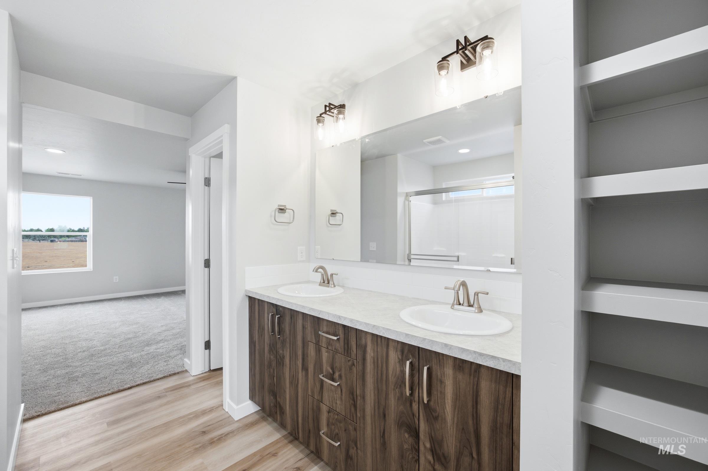 Bathroom featuring a dual vanity with wood-finish cabinetry and light-toned countertops, two undermount sinks with brushed nickel fixtures, and a large wall-mounted mirror