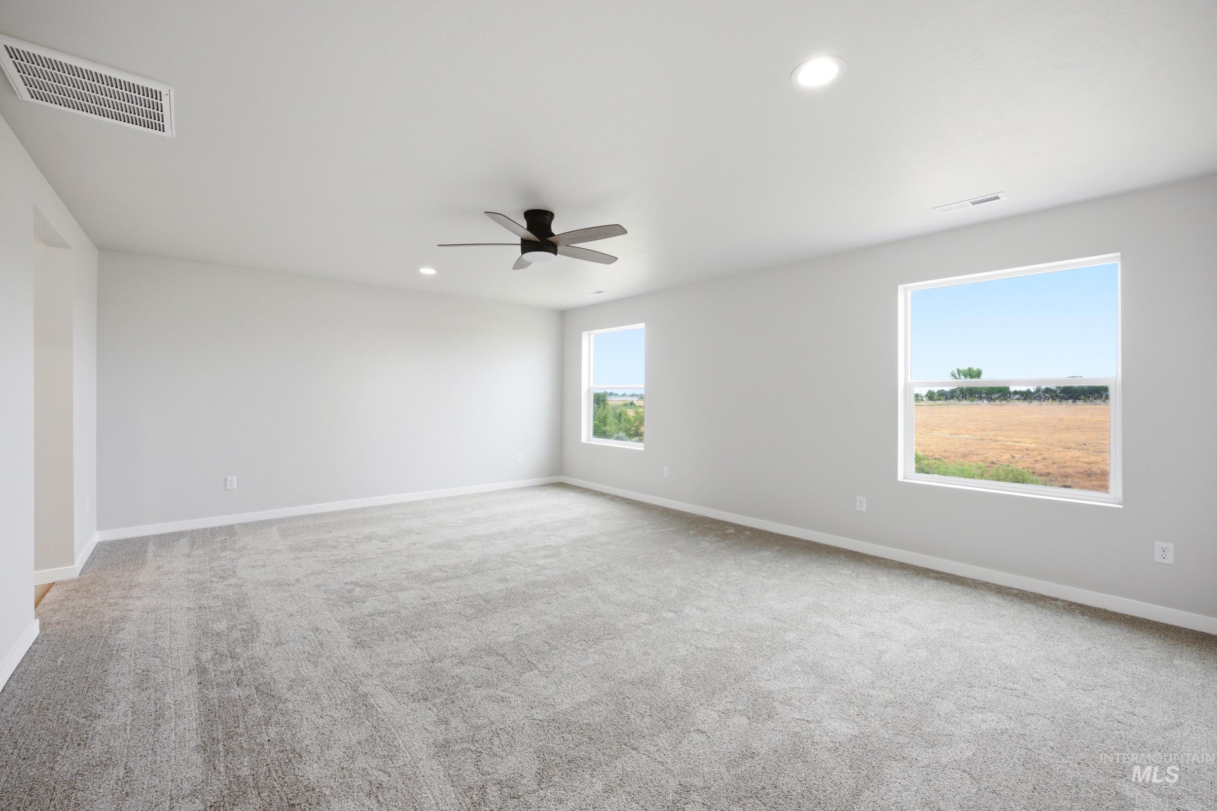 Spacious interior room featuring light gray carpeting, neutral wall finishes, recessed lighting, and a ceiling fan