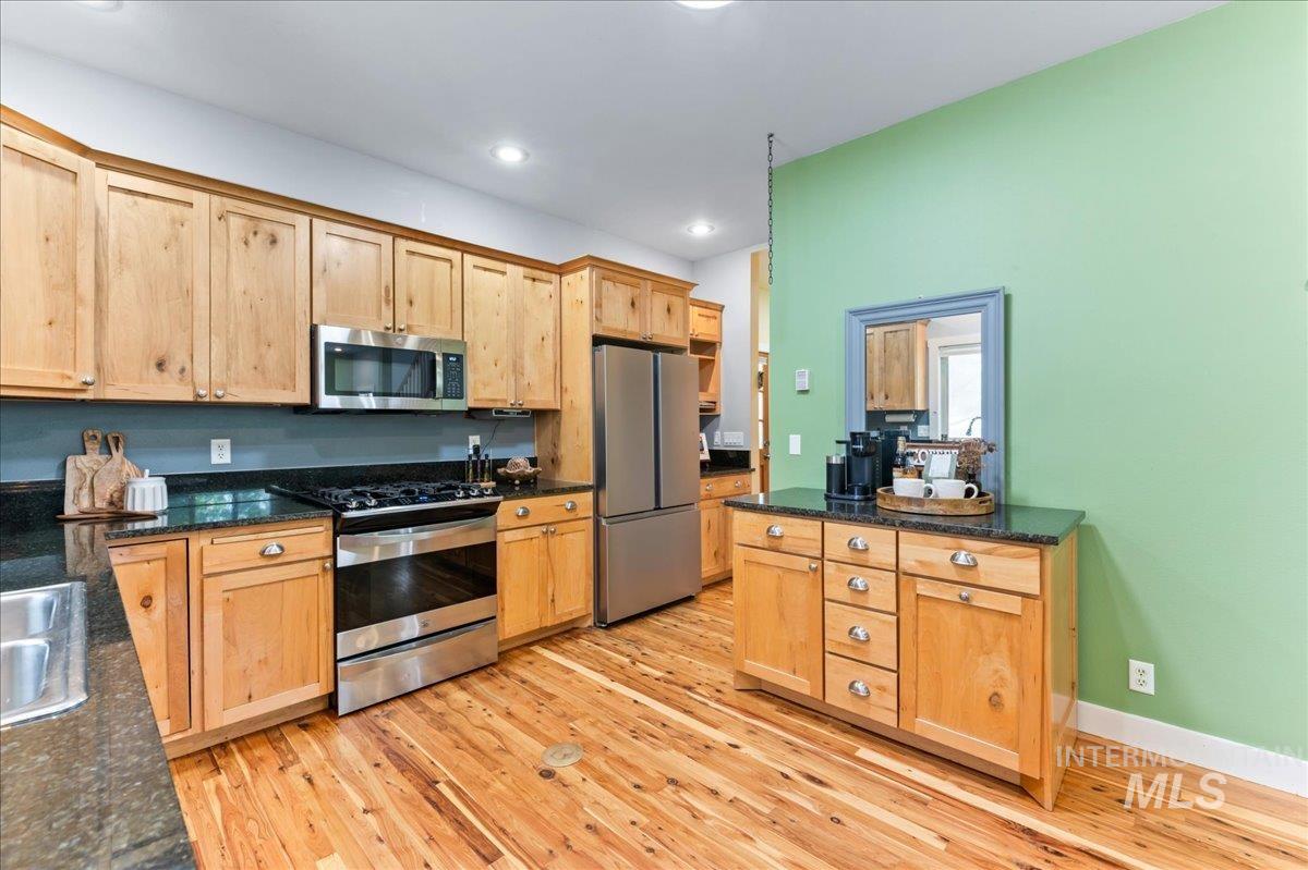Kitchen with appliances with stainless steel finishes, light wood-style floors, dark stone counters, recessed lighting, and light brown cabinetry
