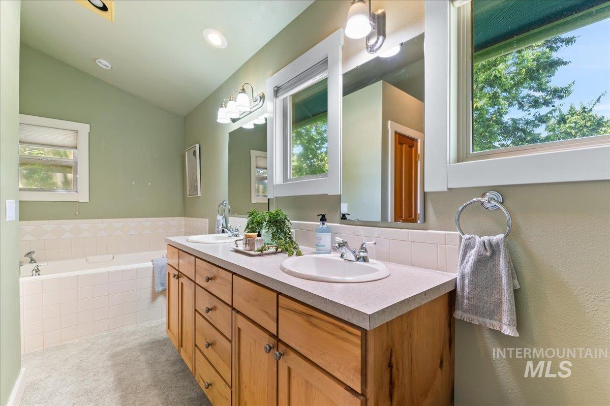 Full bathroom featuring vaulted ceiling, double vanity, healthy amount of natural light, and a bath