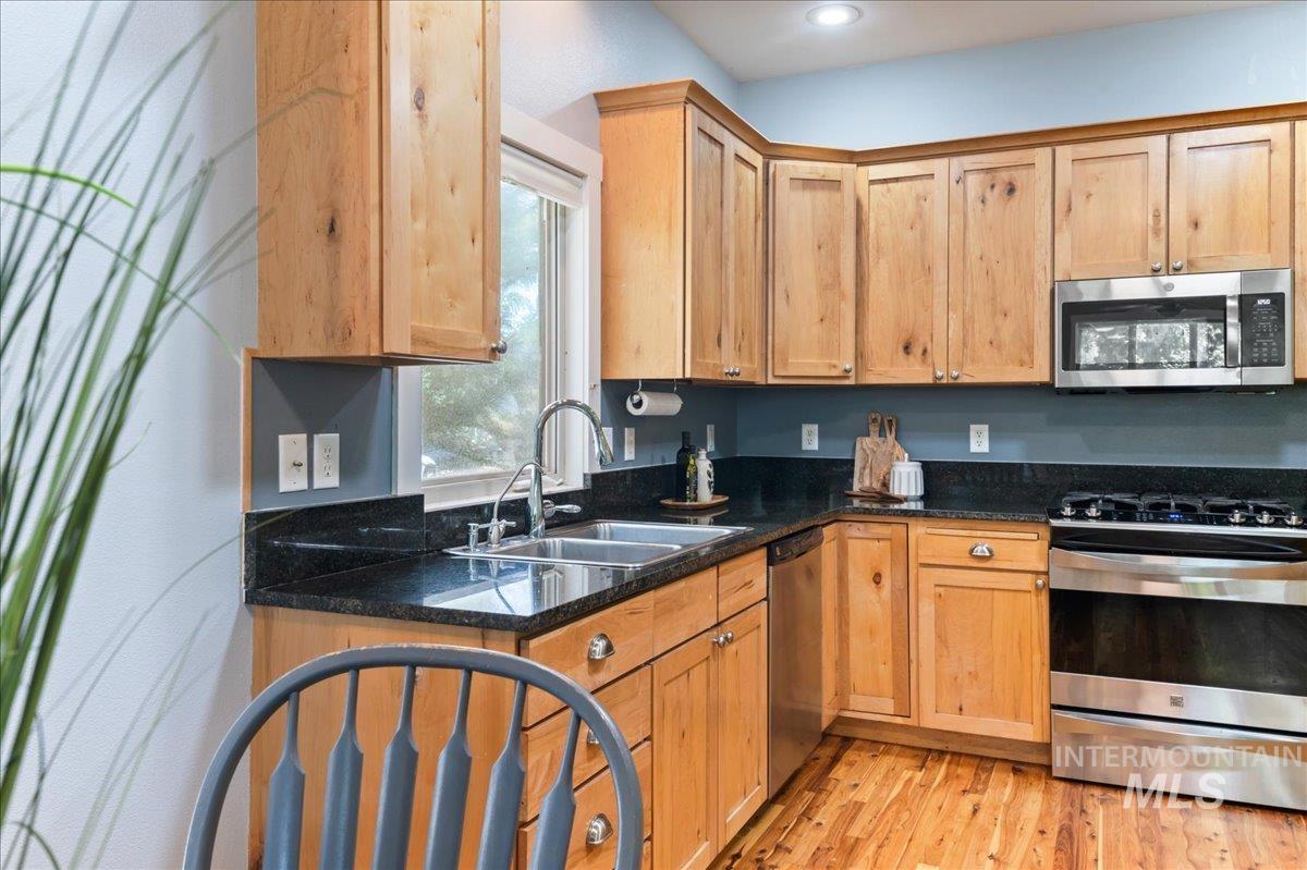 Kitchen with stainless steel appliances, light wood-type flooring, dark stone countertops, and recessed lighting