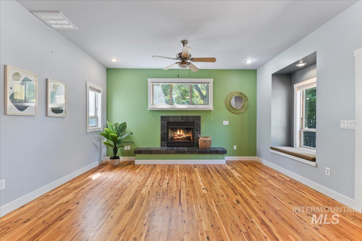 Living area with a tile fireplace, plenty of natural light, hardwood / wood-style floors, and ceiling fan