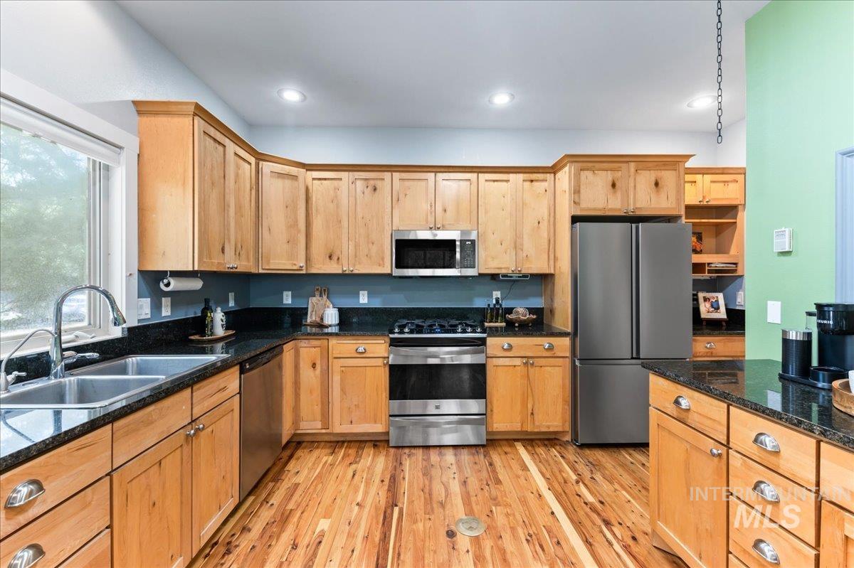 Kitchen with stainless steel appliances, light wood finished floors, dark stone countertops, and recessed lighting