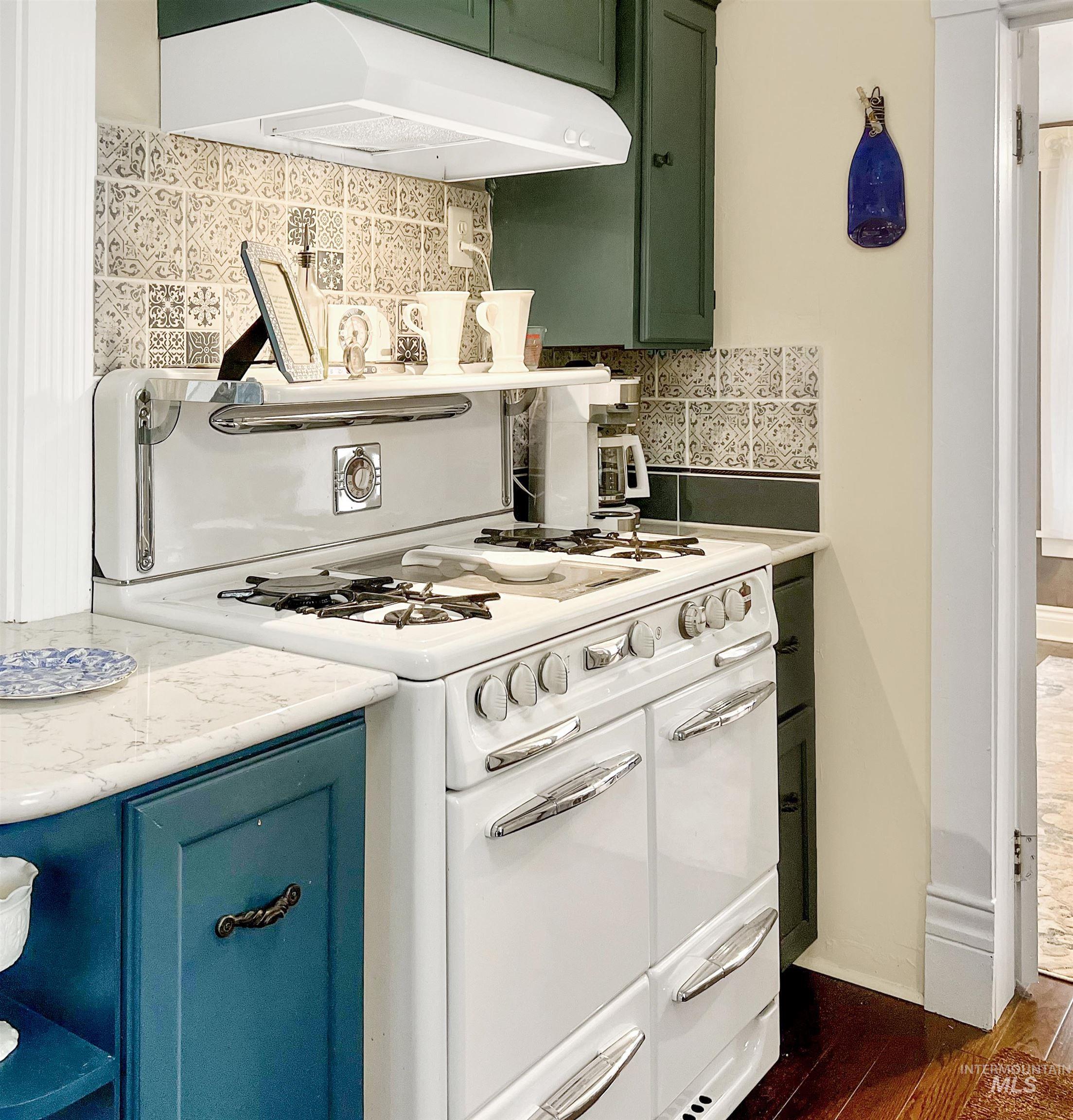 Kitchen with double oven range, decorative backsplash, green cabinets, and dark wood-style flooring