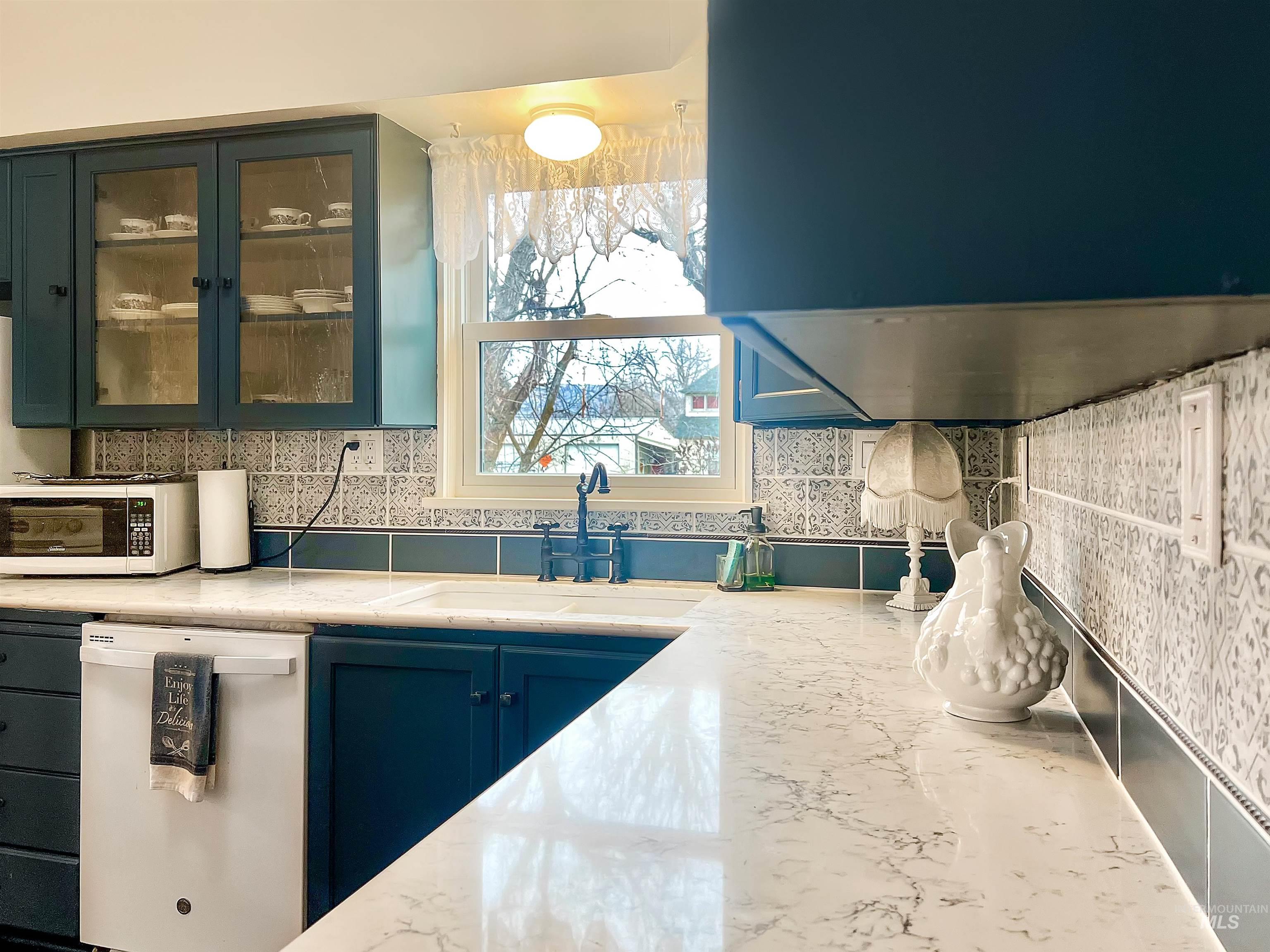 Kitchen featuring white appliances, ventilation hood, decorative backsplash, blue cabinetry, and light stone countertops