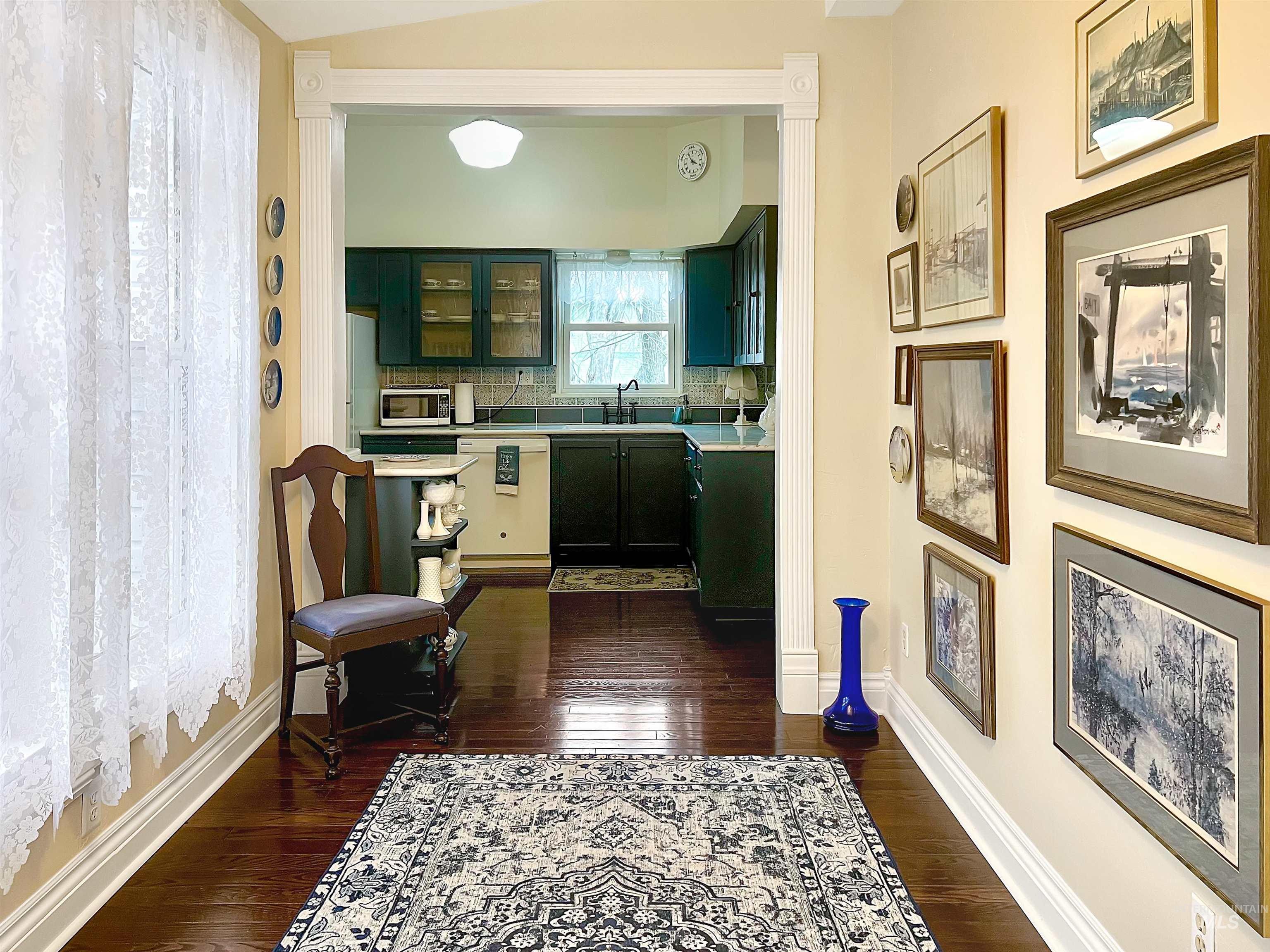 Sunroom leading to kitchen with light countertops, dark wood-type flooring, white appliances, tasteful backsplash, and glass insert cabinets