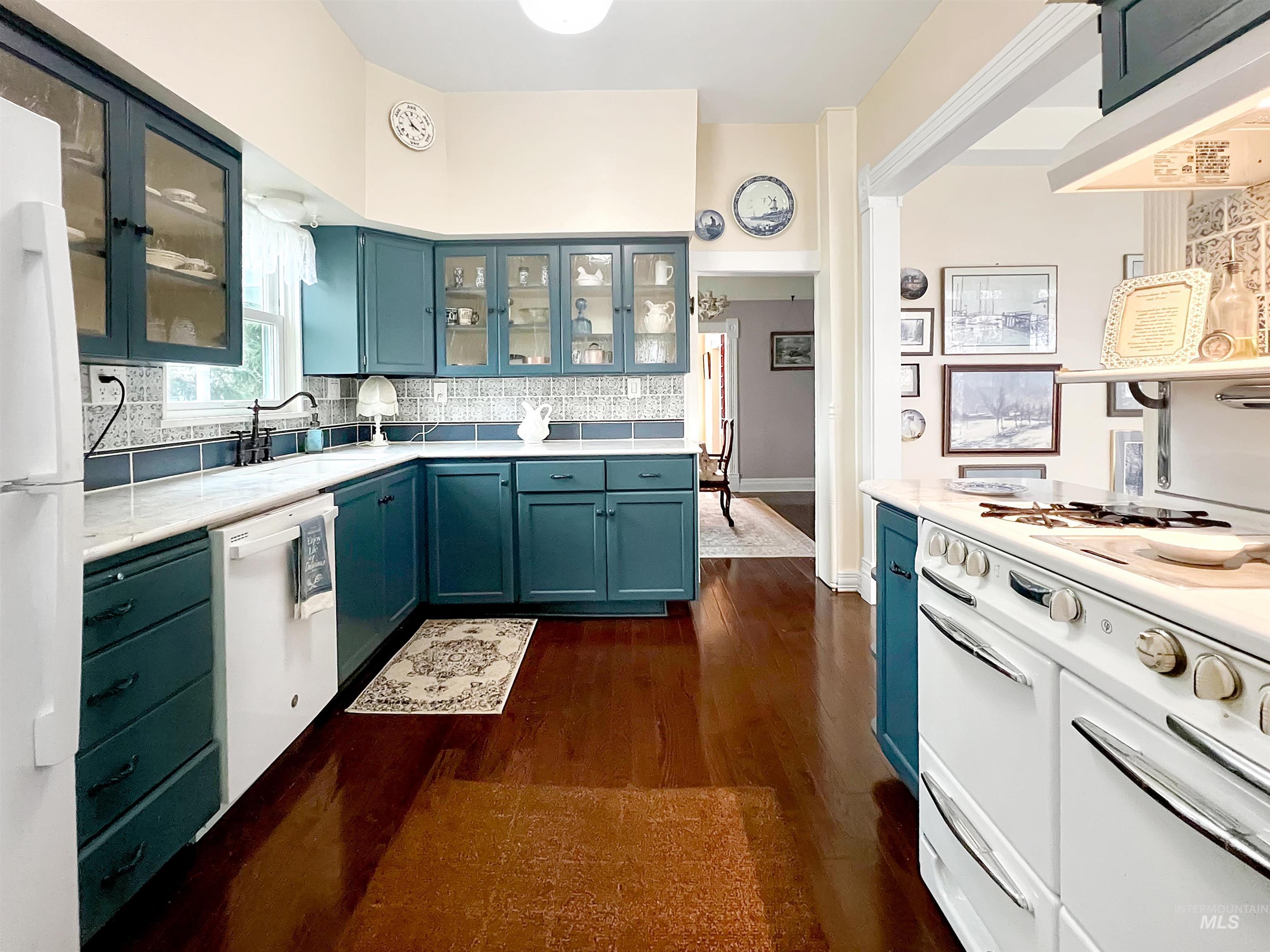 Kitchen featuring blue cabinets, white appliances, glass fronted cabinets, dark wood finished floors, and extractor fan