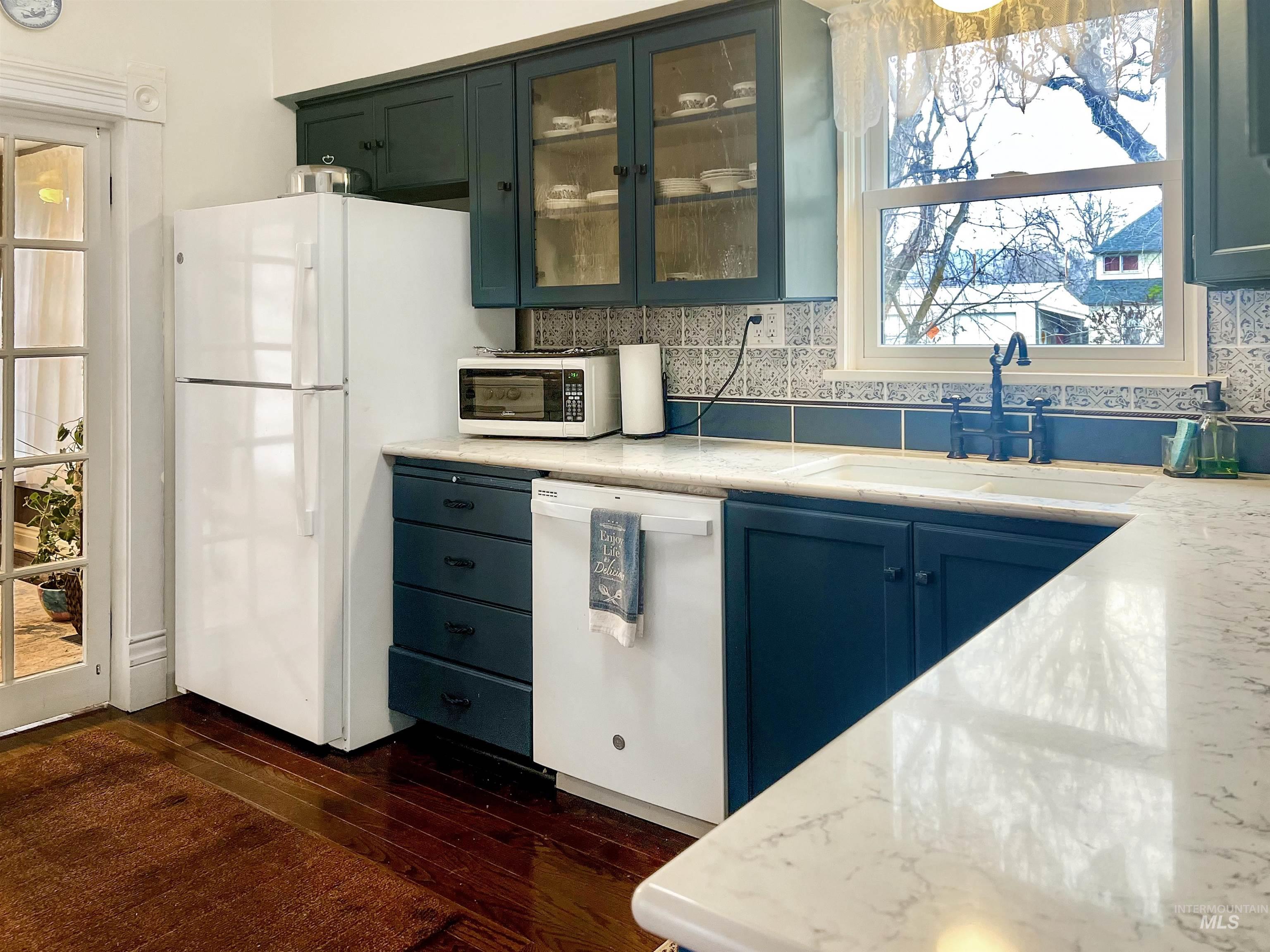 Kitchen featuring glass insert cabinets, decorative backsplash, white appliances, and dark wood finished floors