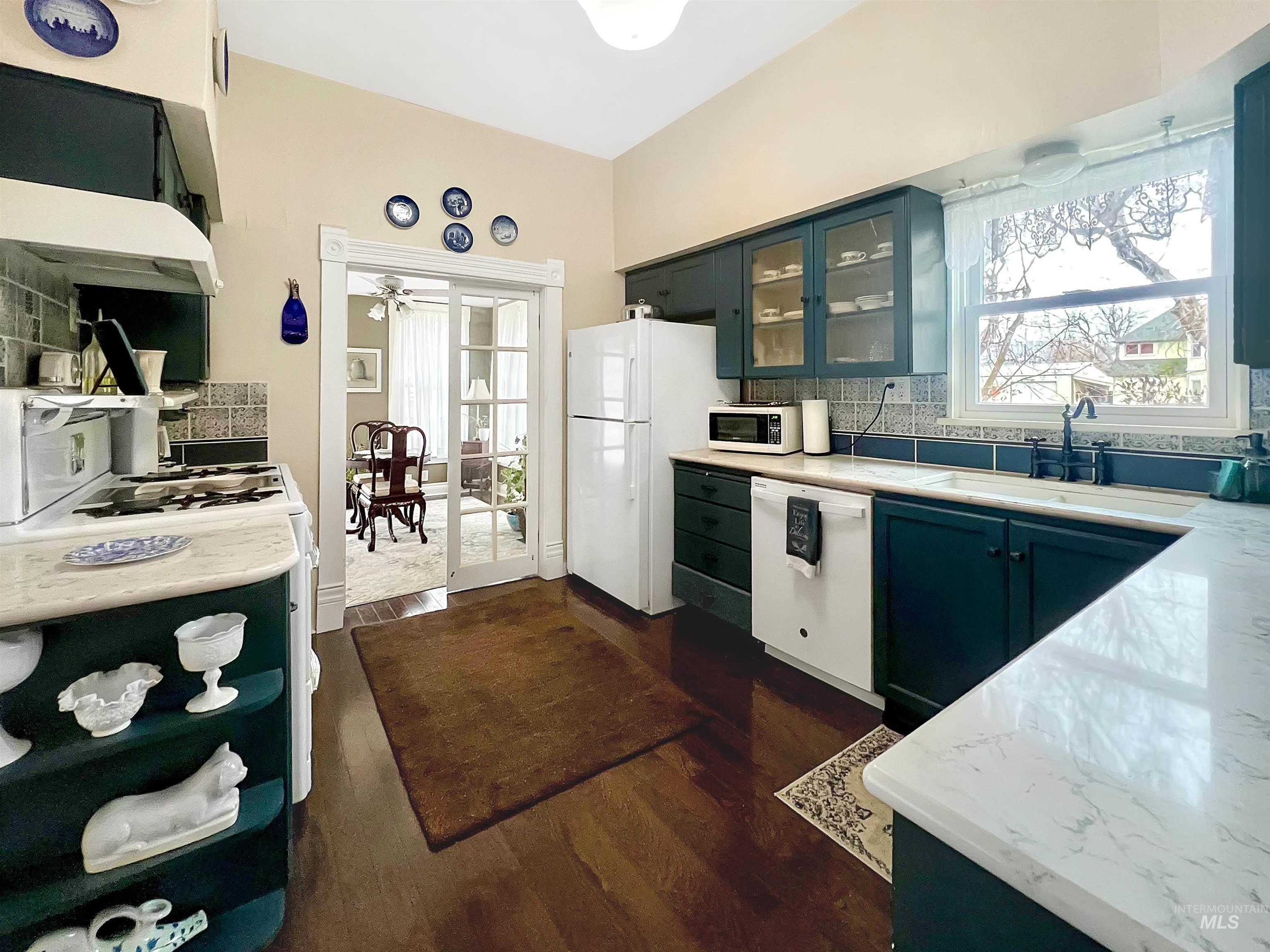 Kitchen with glass fronted cabinets, backsplash, white appliances, and dark wood-type flooring