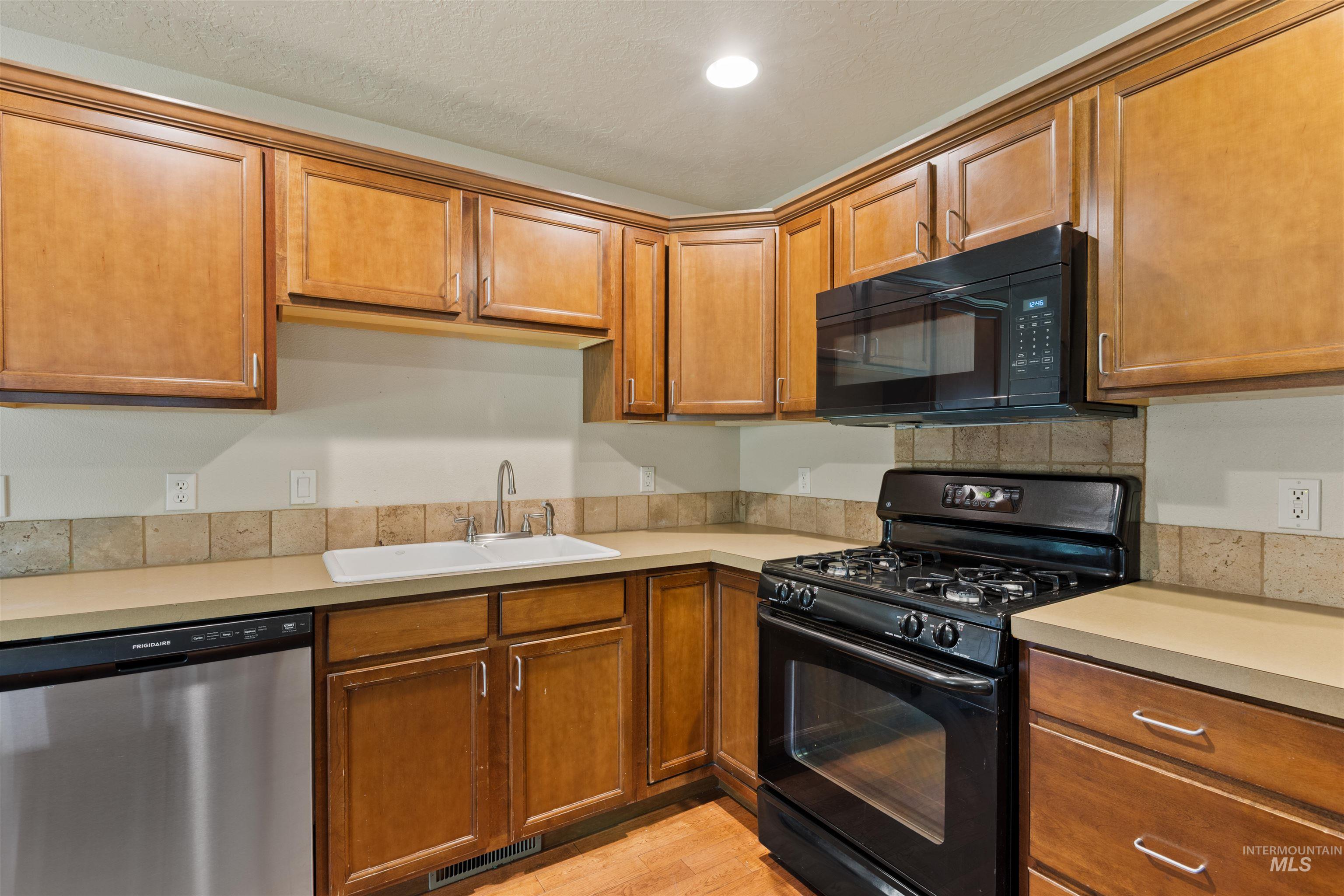 Kitchen with black appliances, brown cabinetry, light countertops, light wood-style floors, and recessed lighting