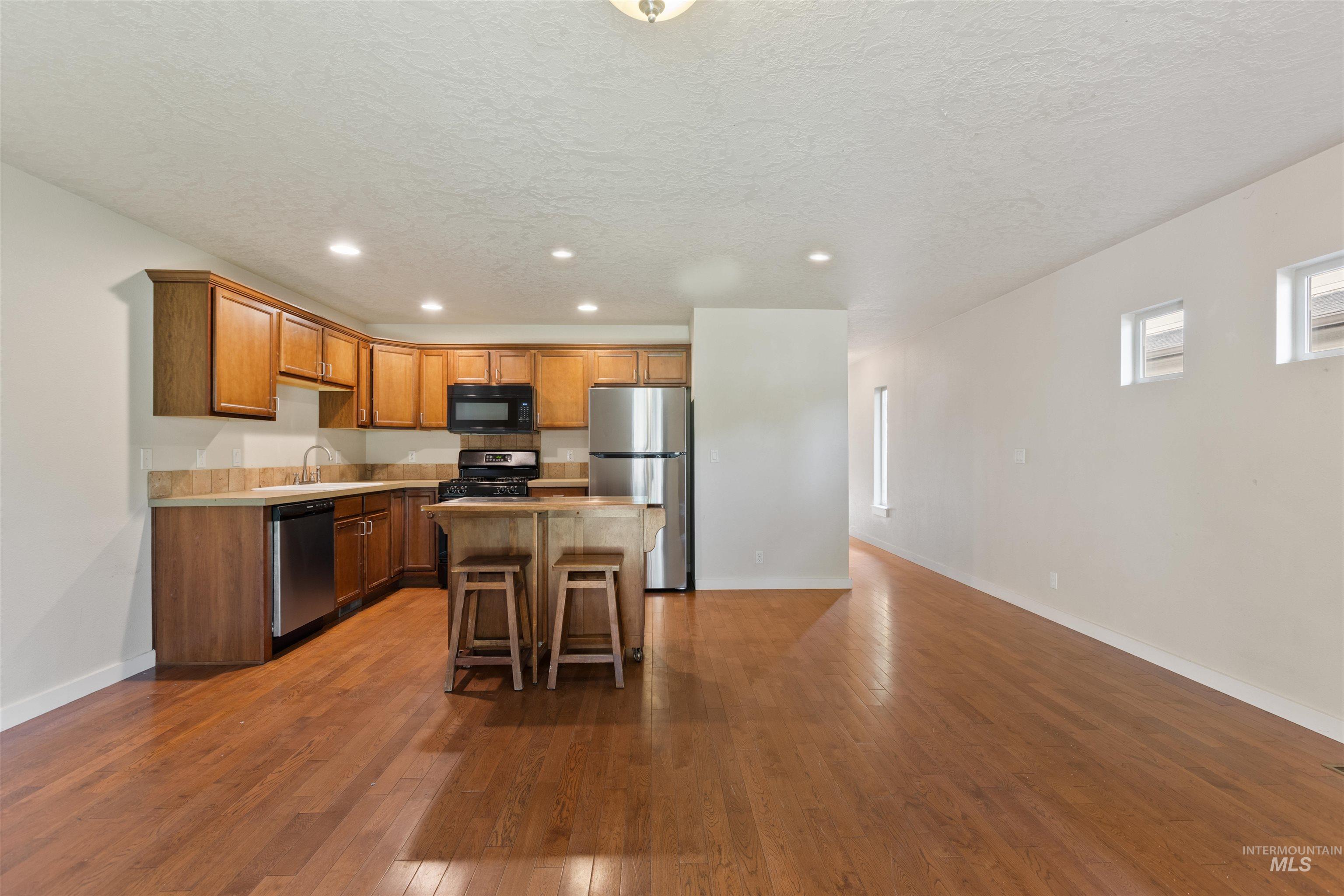 Kitchen with recessed lighting, brown cabinets, black appliances, light countertops, and dark wood-style floors