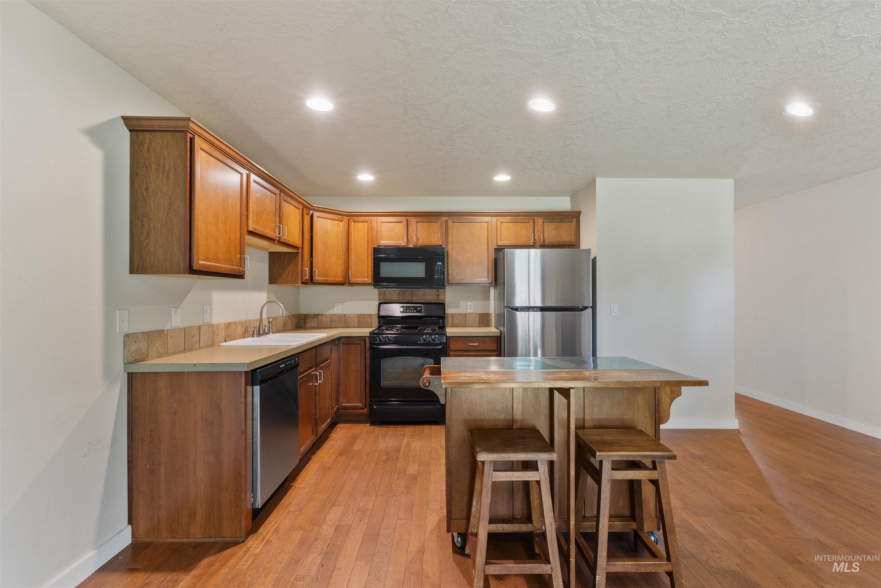 Kitchen featuring recessed lighting, black appliances, brown cabinetry, a kitchen breakfast bar, and light countertops