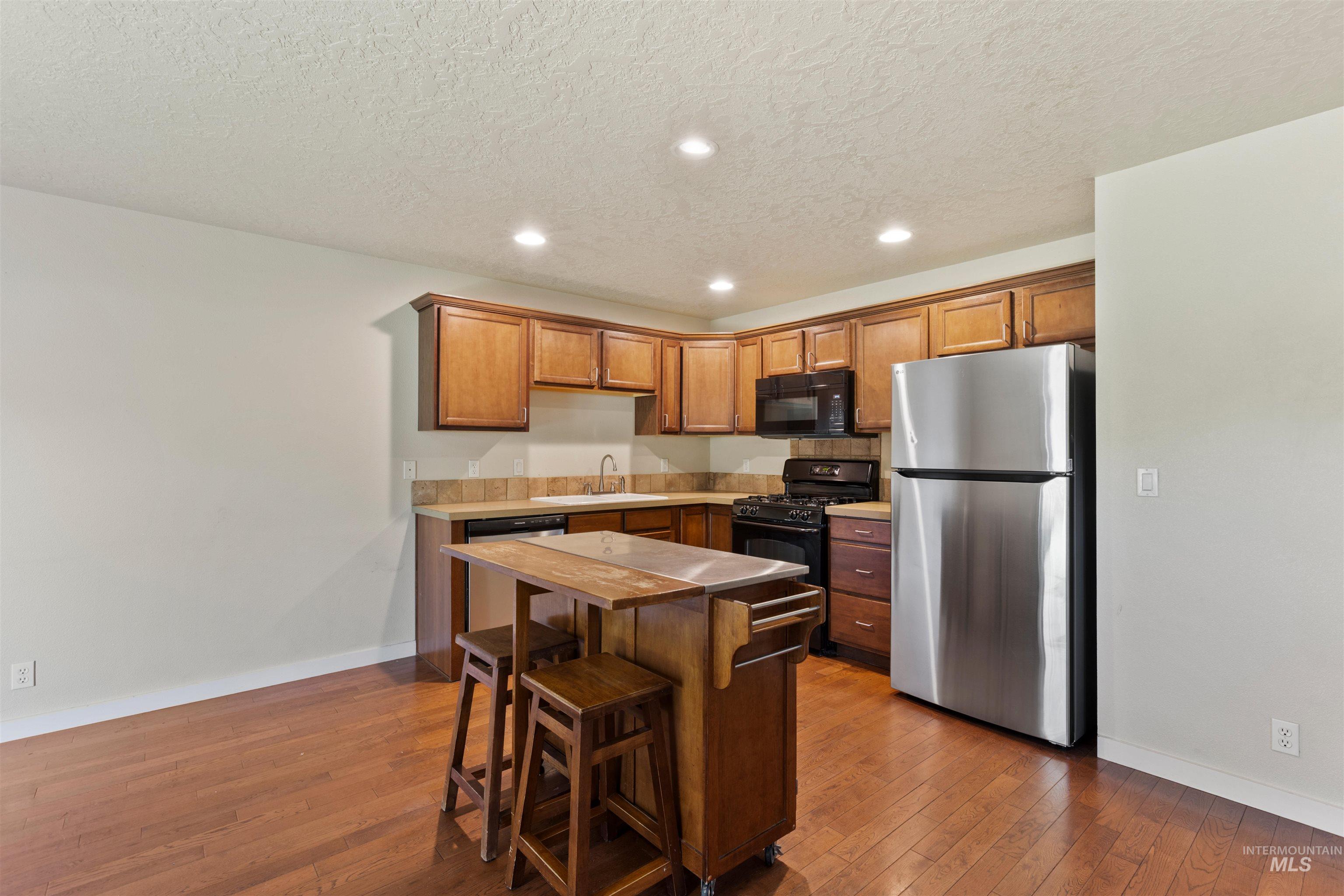 Kitchen with black appliances, recessed lighting, a kitchen breakfast bar, dark wood finished floors, and brown cabinets