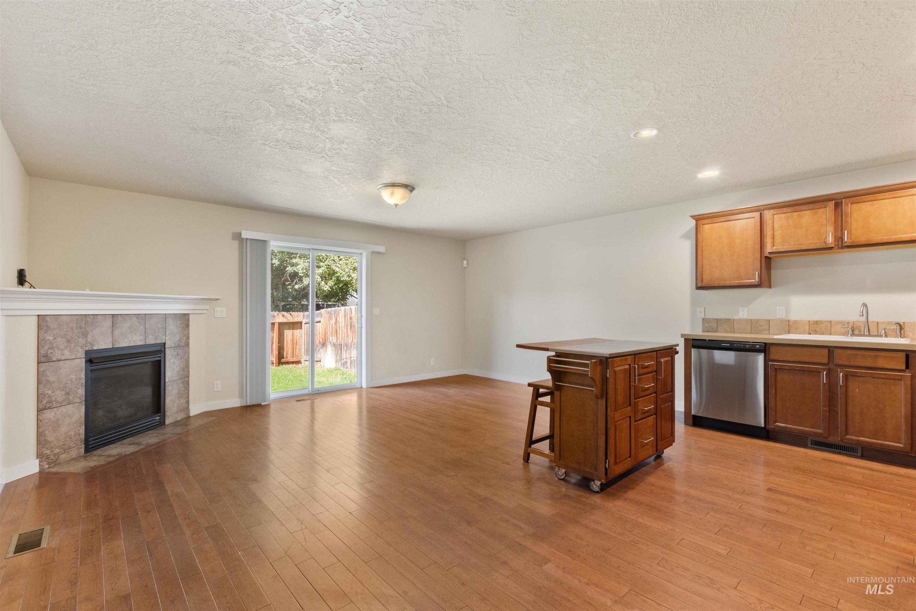 Kitchen featuring a tiled fireplace, open floor plan, a kitchen breakfast bar, brown cabinets, and a textured ceiling