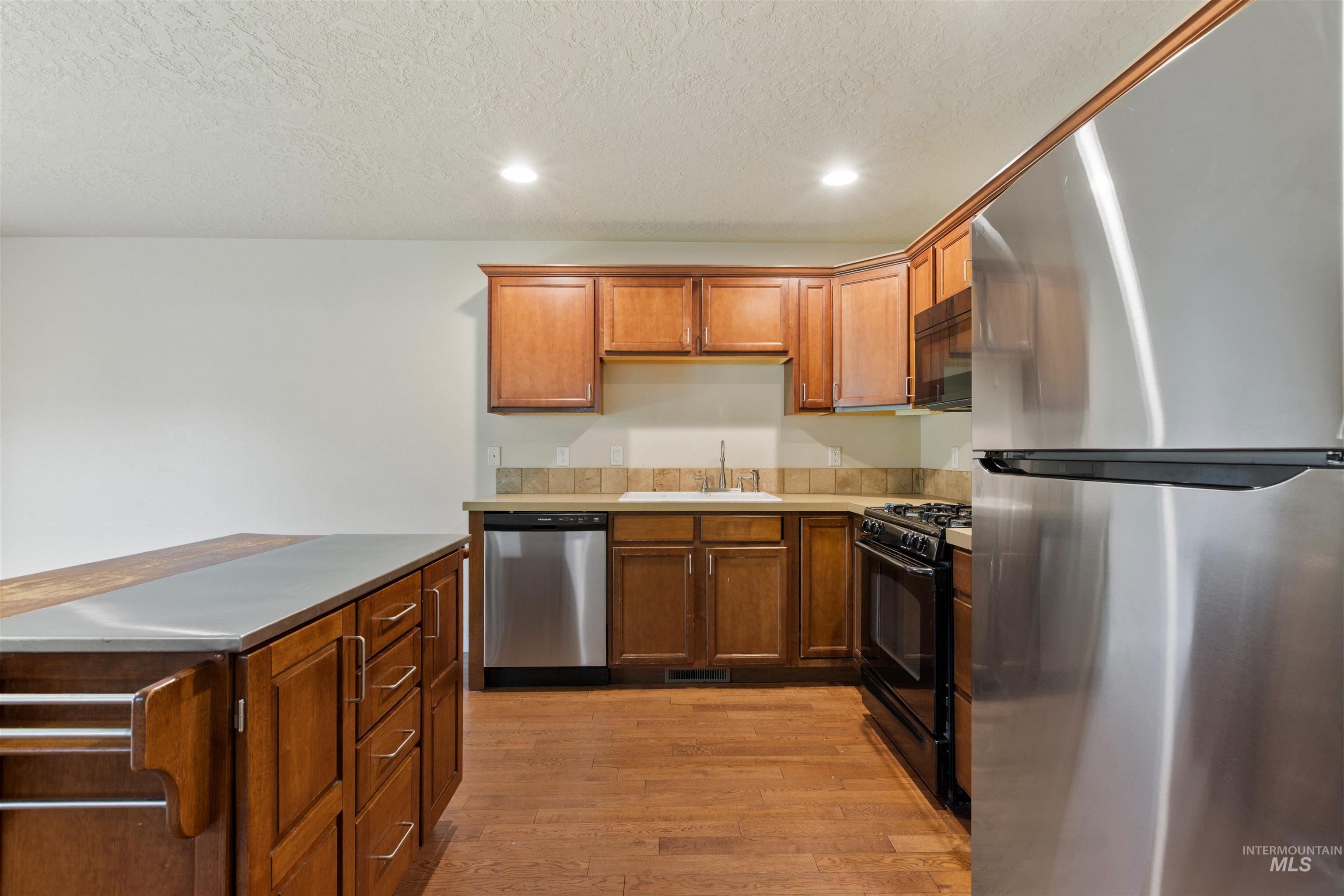 Kitchen with black appliances, light countertops, light wood-type flooring, a textured ceiling, and brown cabinetry