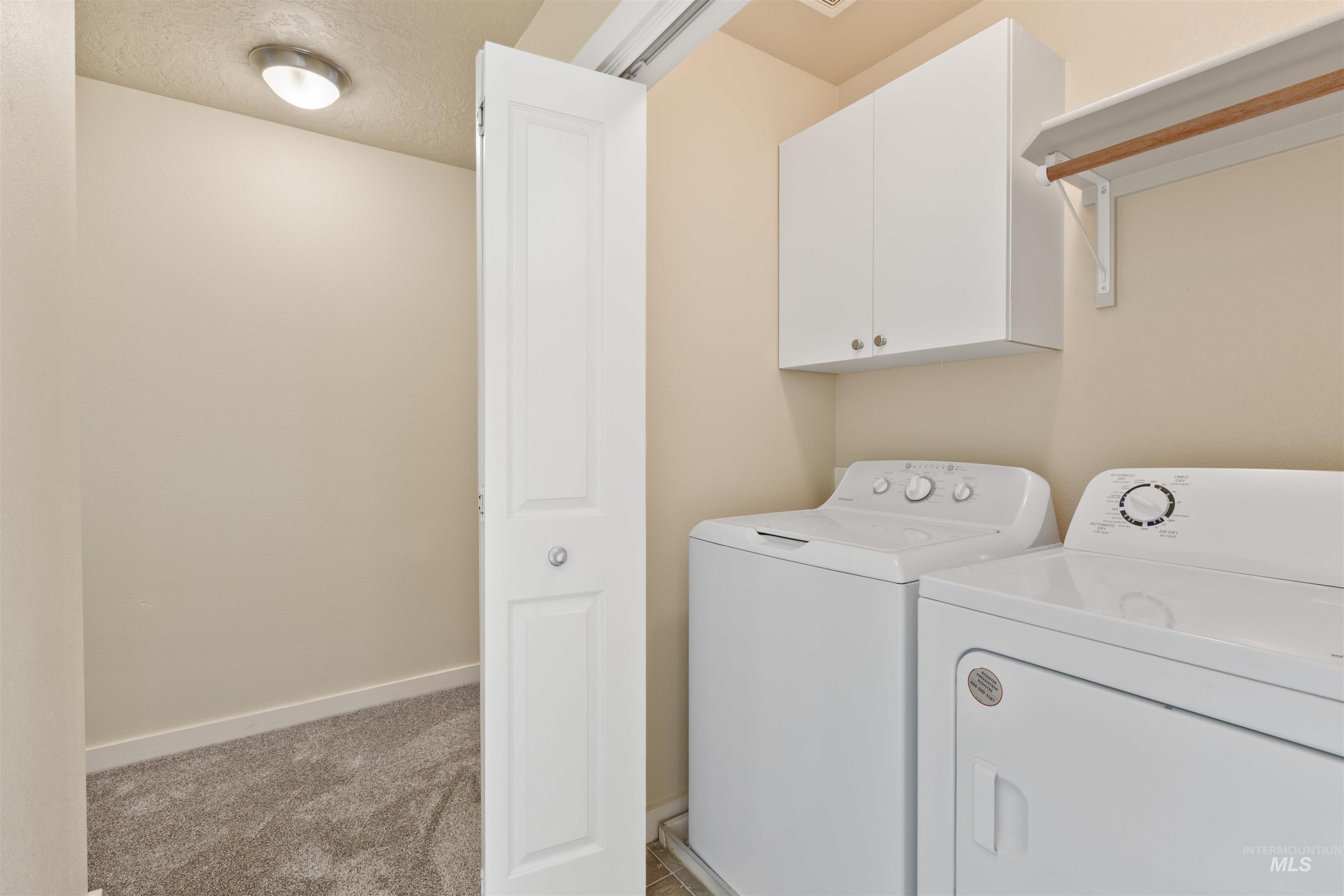 Laundry area with washer and dryer, a textured ceiling, cabinet space, and light carpet