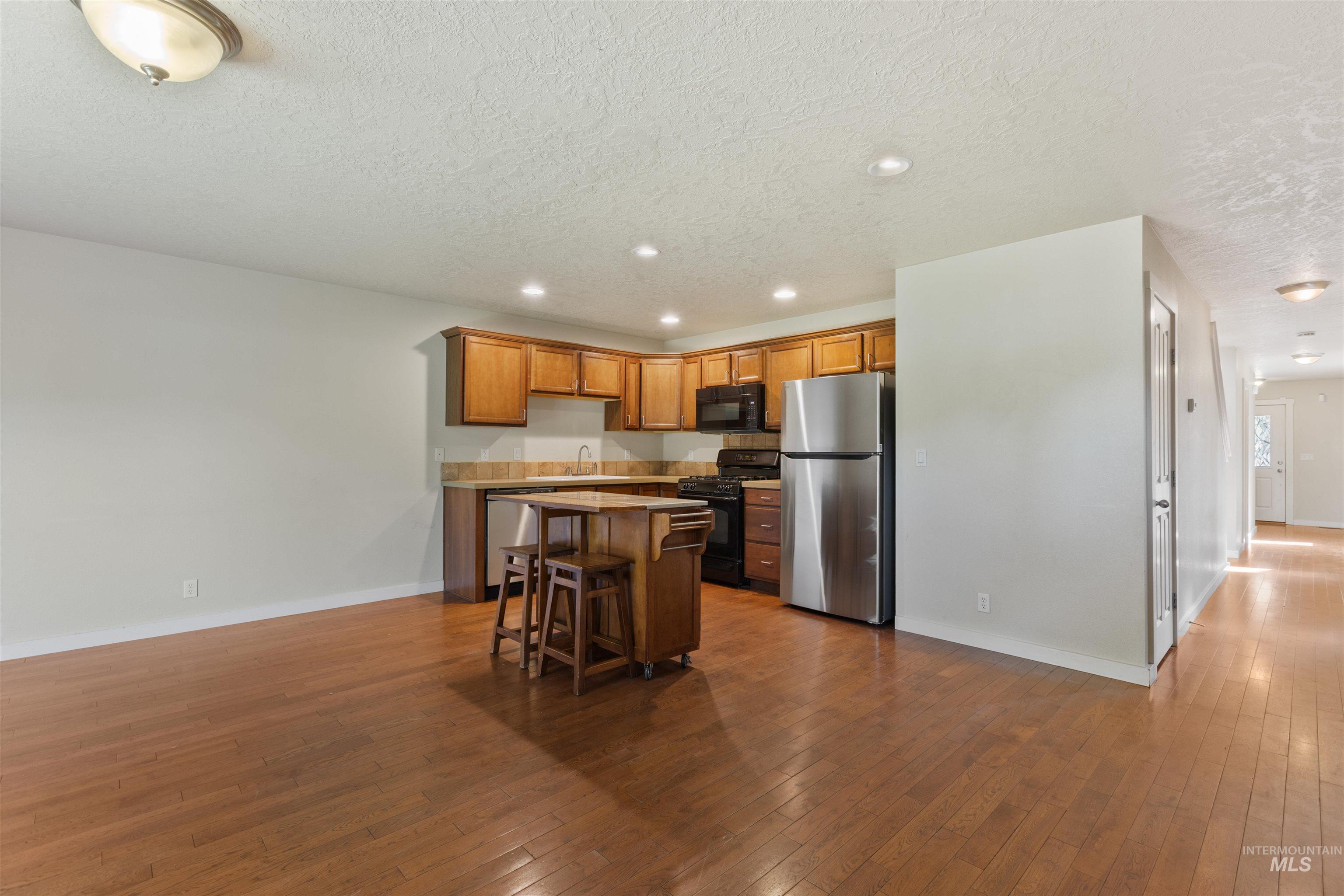 Kitchen with recessed lighting, black appliances, dark wood-type flooring, light countertops, and a kitchen breakfast bar