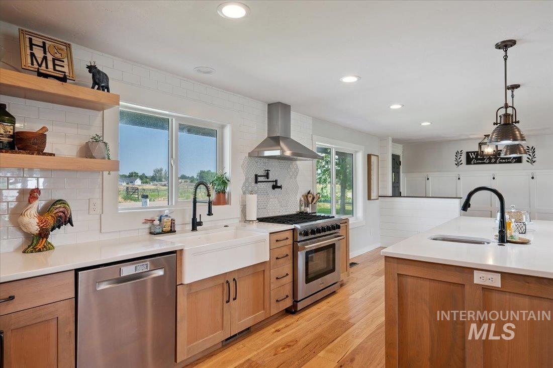 Kitchen with tasteful backsplash, stainless steel appliances, light wood-type flooring, decorative light fixtures, and light stone countertops
