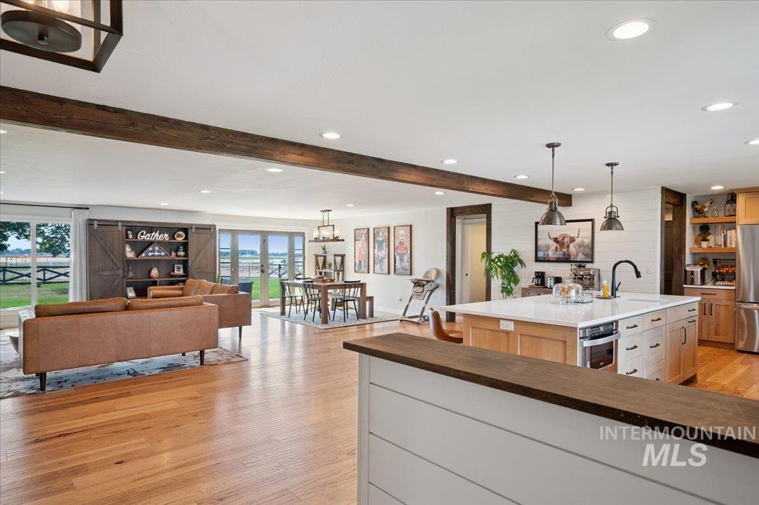 Two tone kitchen with light wood-style flooring, hanging light fixtures, open floor plan, dual tone cabinets, and stainless steel appliances