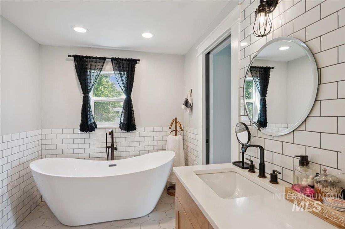Full bath featuring tile walls, vanity, wainscoting, a freestanding bath, and light tile patterned flooring