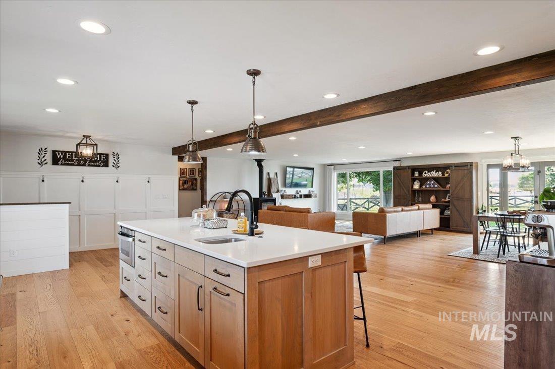 Two tone kitchen with open floor plan, hanging light fixtures, light wood-style floors, a breakfast bar, and an island with sink