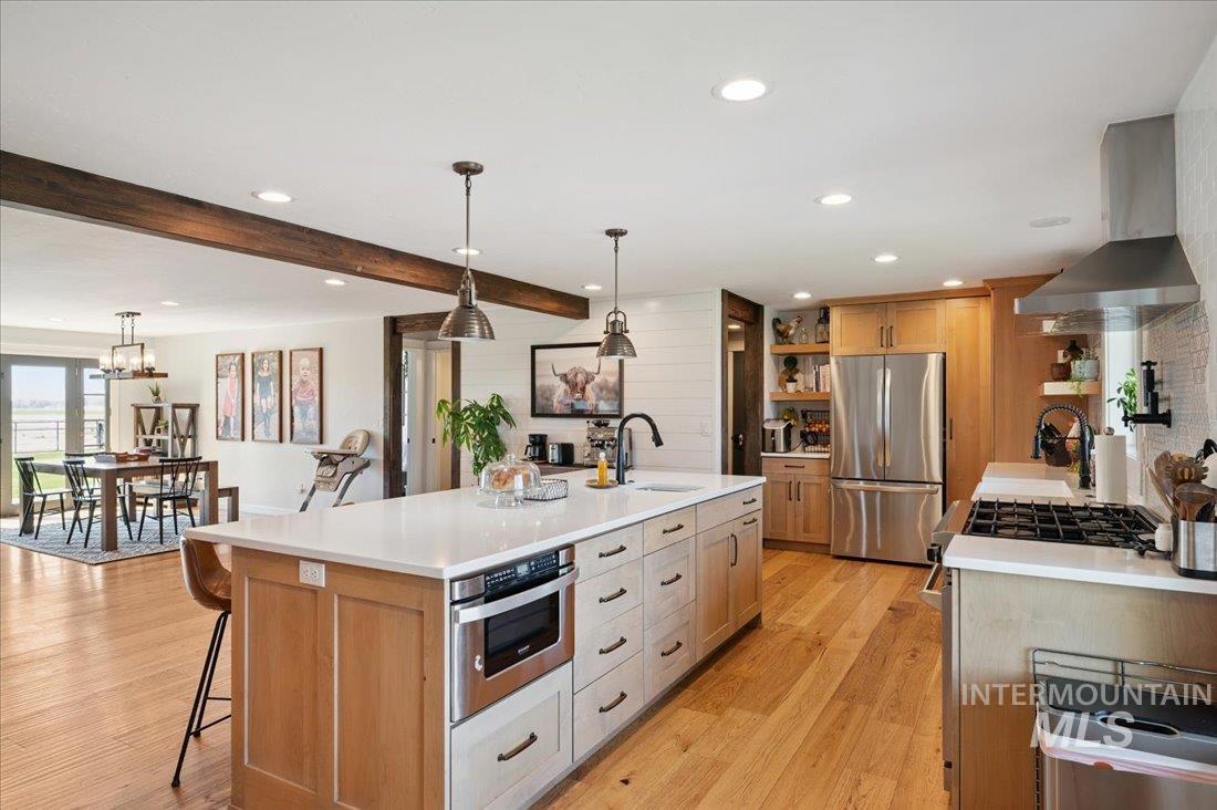 Kitchen featuring stainless steel appliances, exhaust hood, hanging light fixtures, light wood finished floors, and wood walls