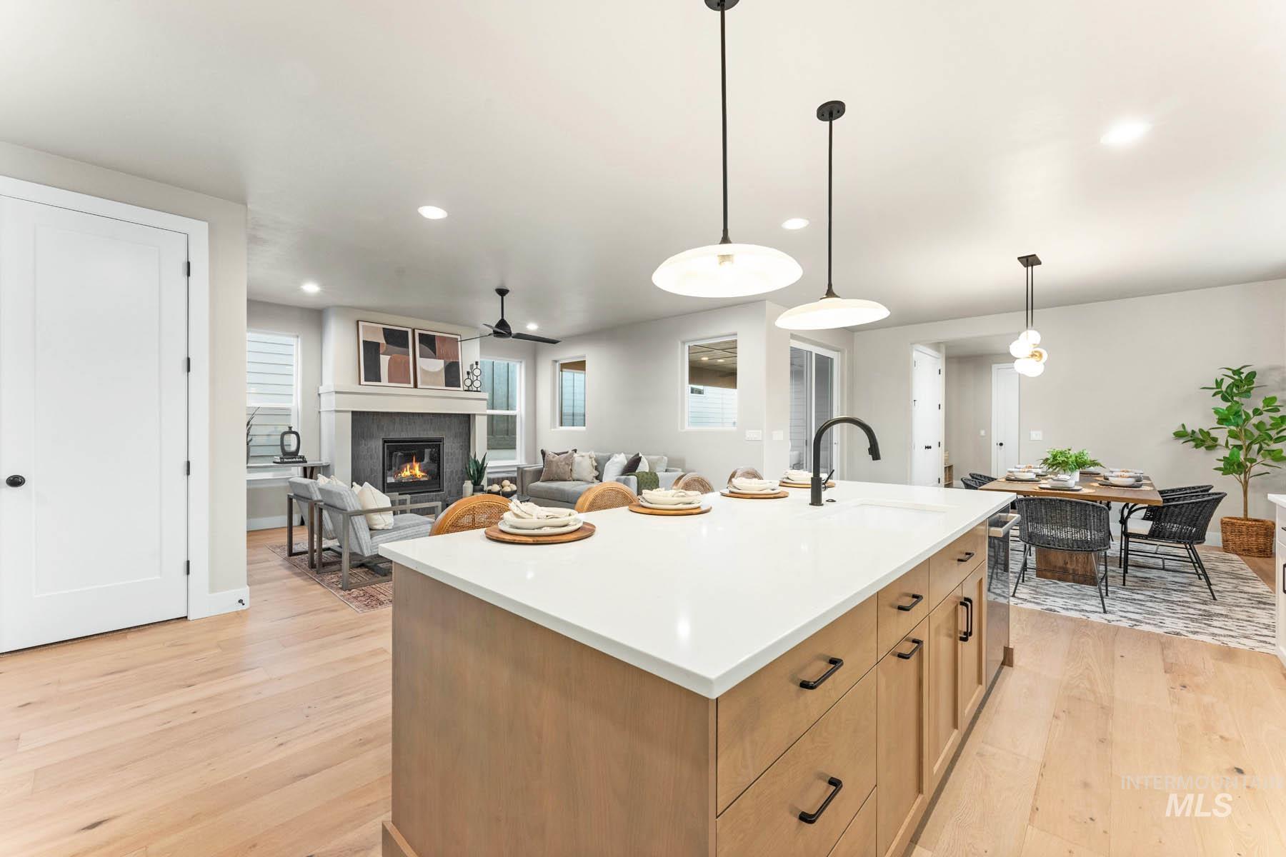 Kitchen featuring an island with sink, a glass covered fireplace, light wood-style floors, decorative light fixtures, and open floor plan