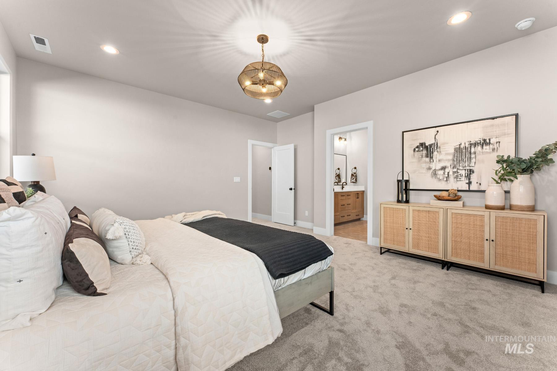 Bedroom with light colored carpet, ensuite bathroom, and hanging lights