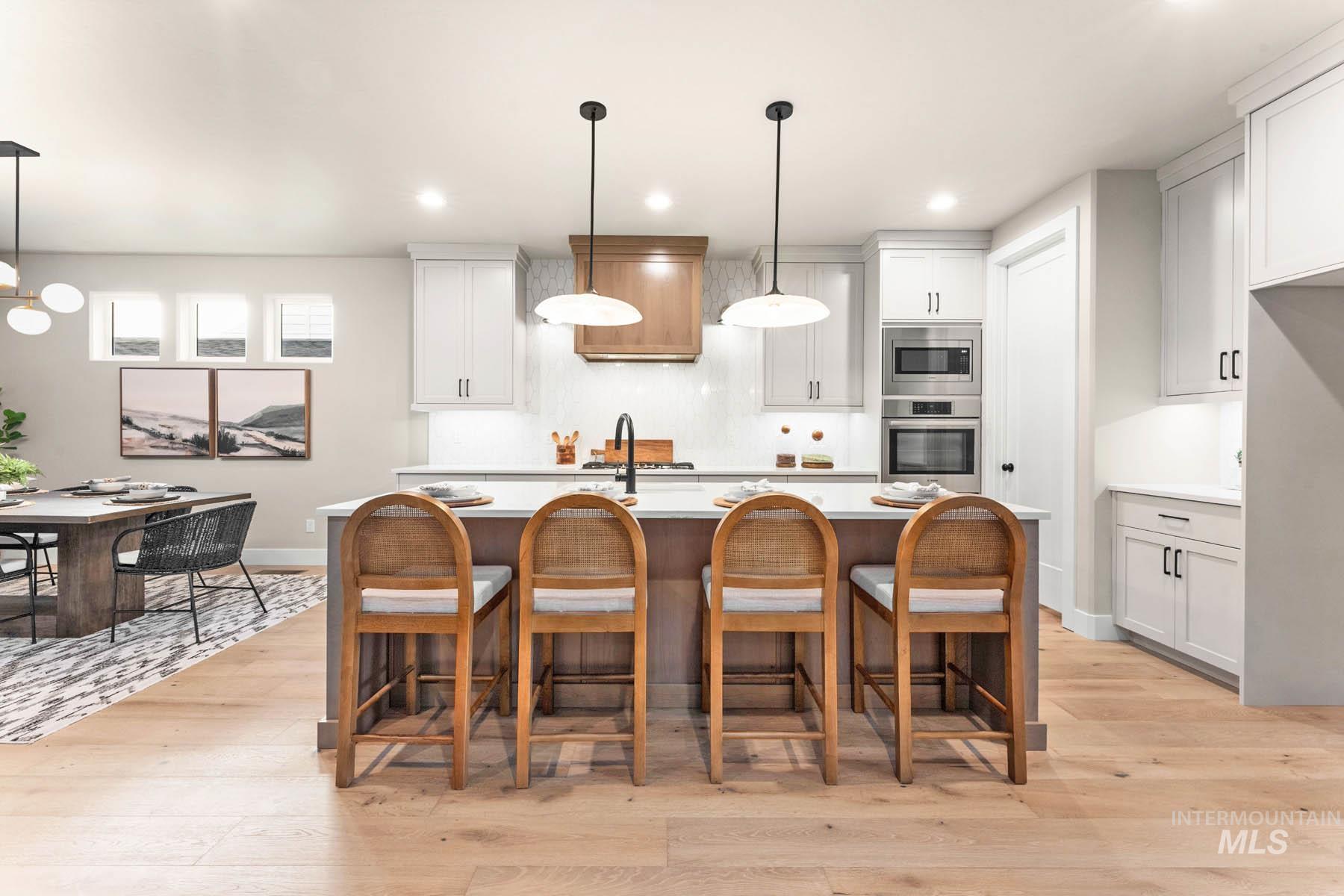 Kitchen with a breakfast bar, a kitchen island with sink, light wood-style floors, and white cabinetry
