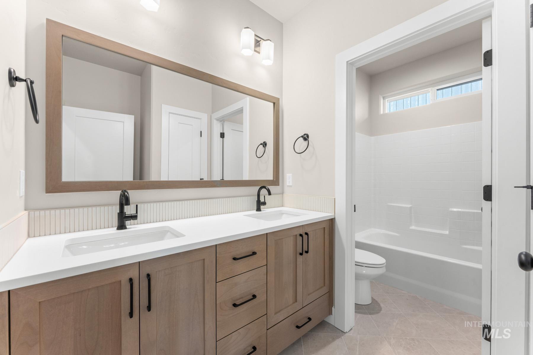 Full bath featuring double vanity, light tile patterned flooring, and bathing tub / shower combination