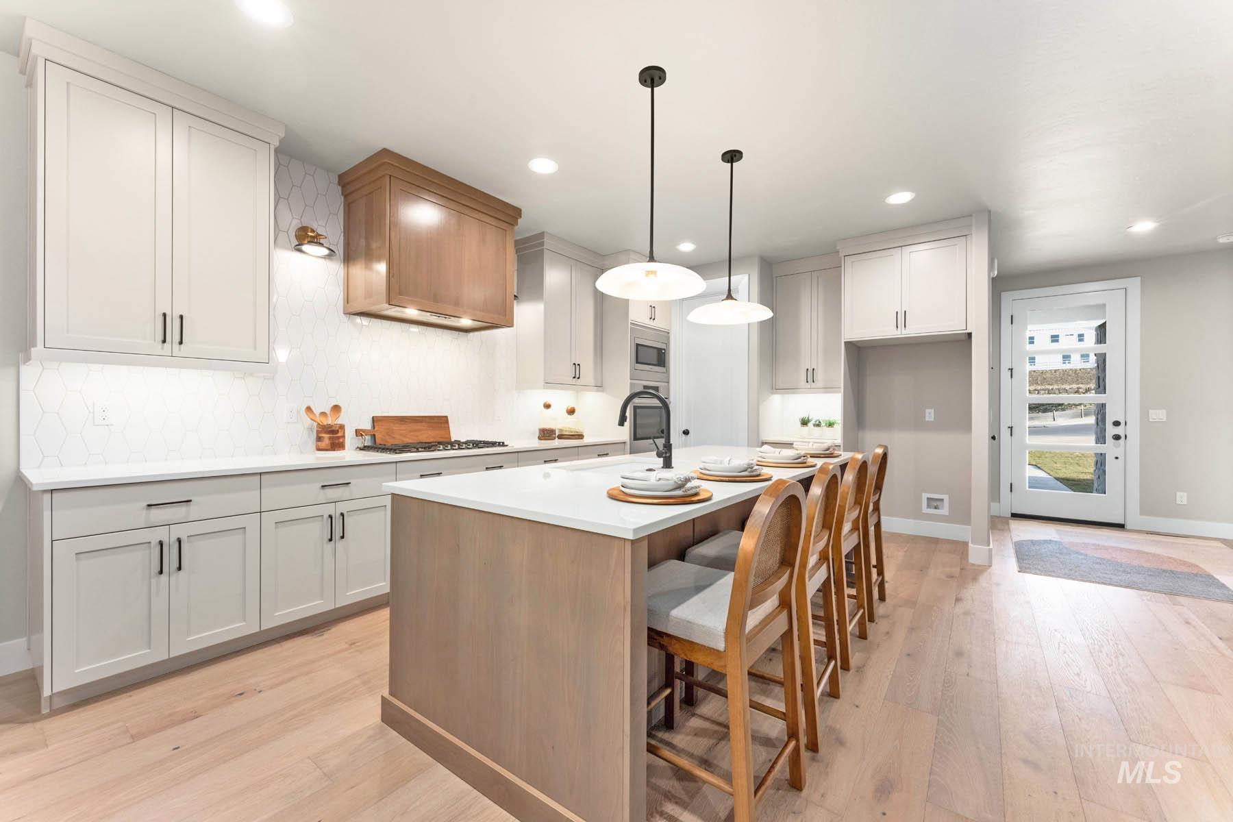 Kitchen with a kitchen breakfast bar, an island with sink, two tone color scheme, light wood-style flooring, and decorative light fixtures