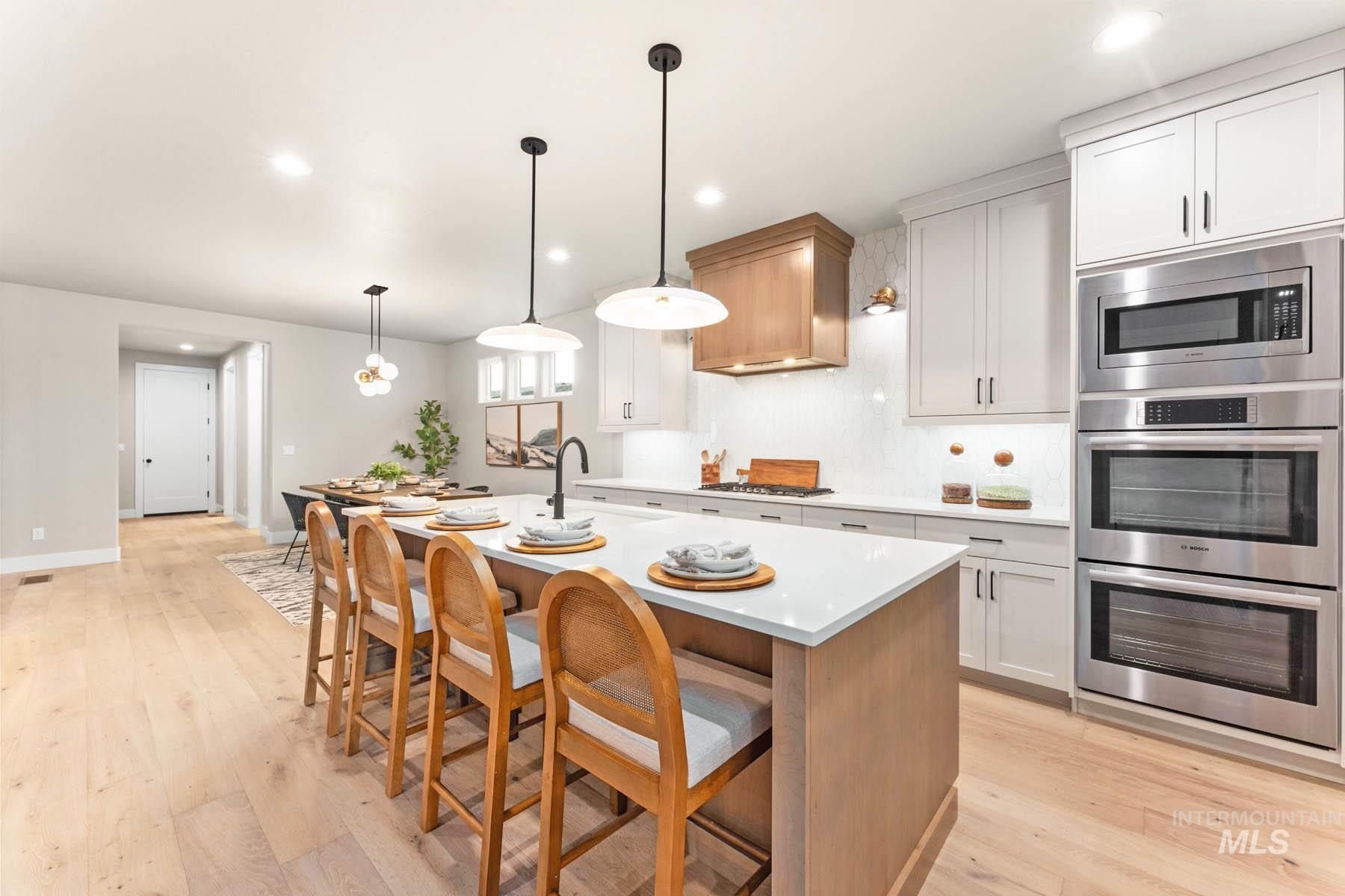 Kitchen featuring stainless steel appliances, a kitchen breakfast bar, an island with sink, light wood finished floors, and two tone cabinetry