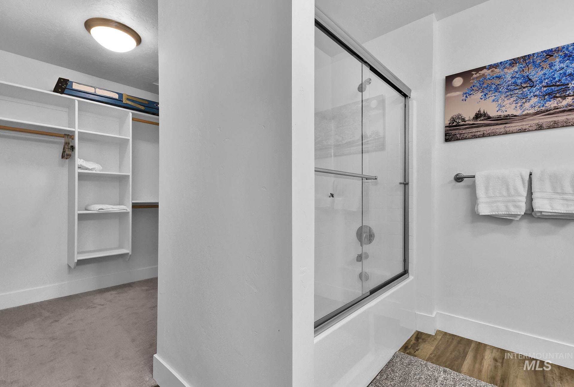 Bathroom featuring enclosed tub / shower combo, a spacious closet, and light wood finished floors