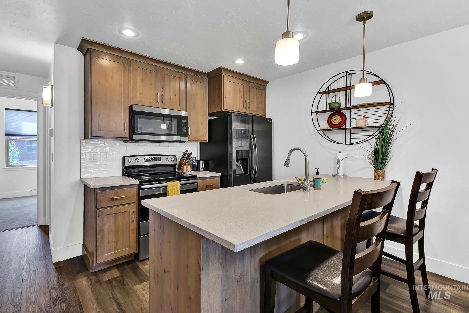 Kitchen with stainless steel appliances, wood finish cabinets, dark wood-type flooring, a center island with sink, and decorative backsplash