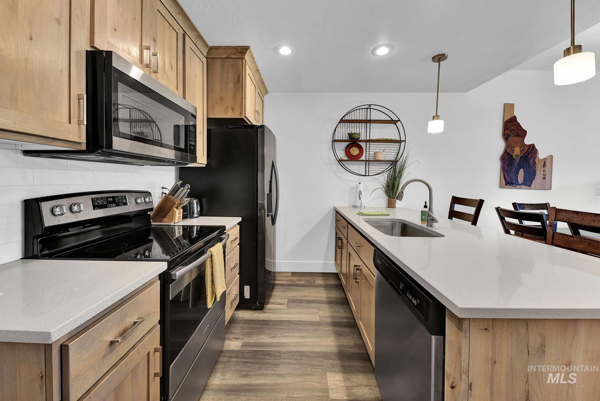 Kitchen with stainless steel appliances, light stone counters, a peninsula, a breakfast bar, and dark wood-style flooring