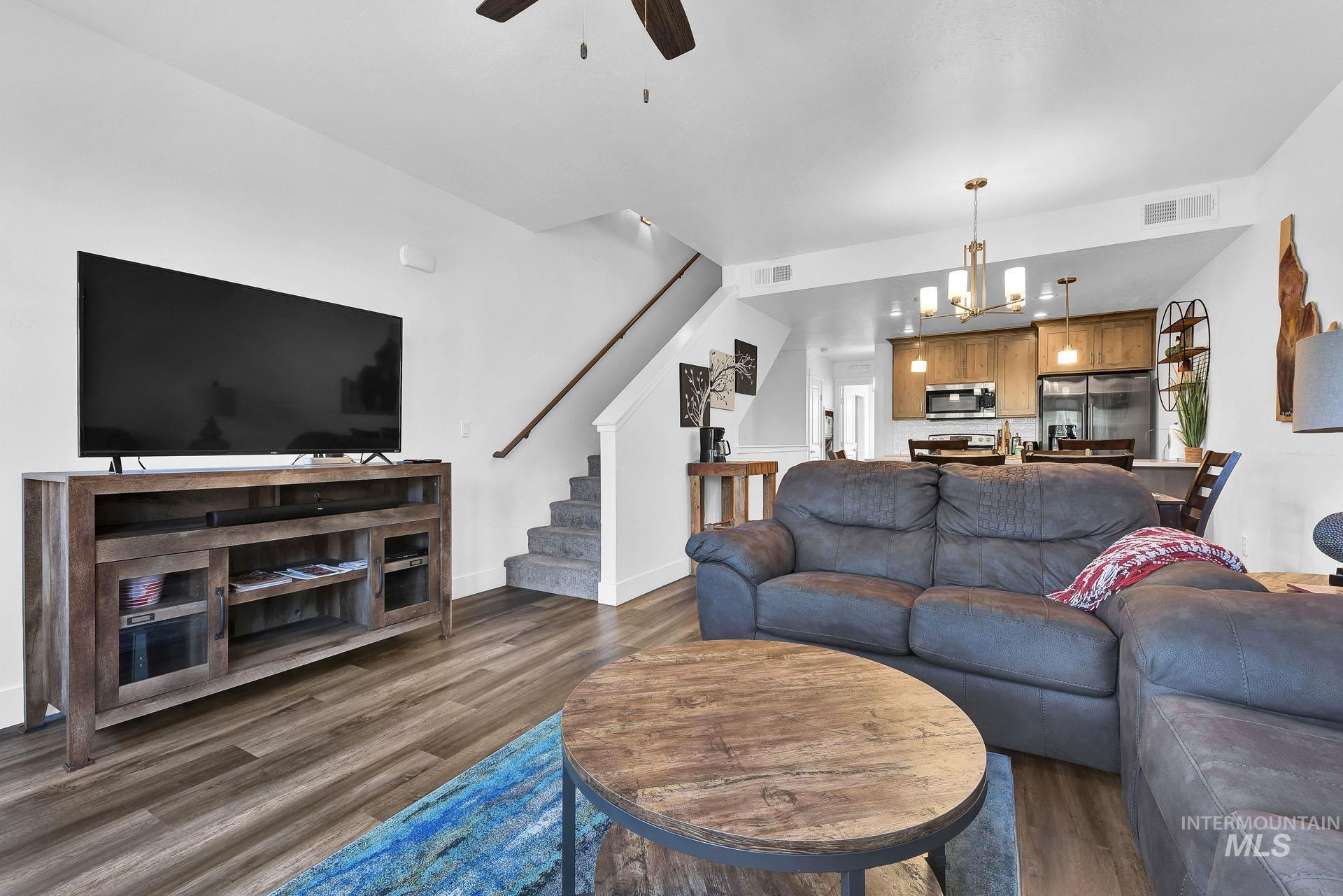 Living room featuring a ceiling fan, dark wood-style flooring, and hanging lights