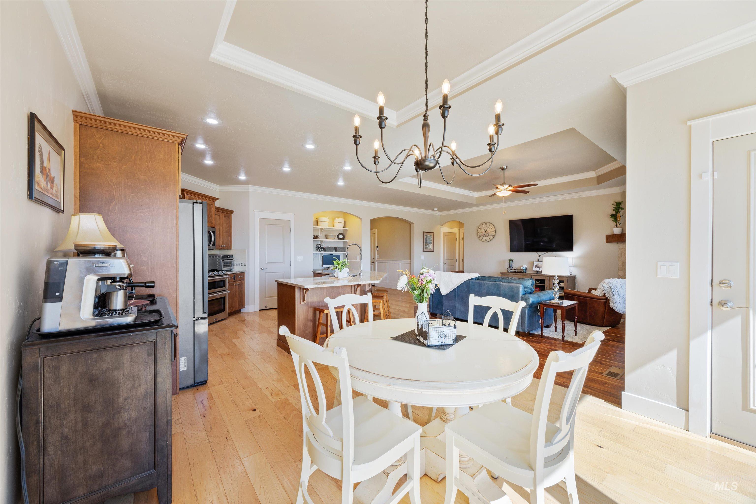 Dining area with a tray ceiling, arched walkways, light wood-style floors, ornamental molding, and a chandelier
