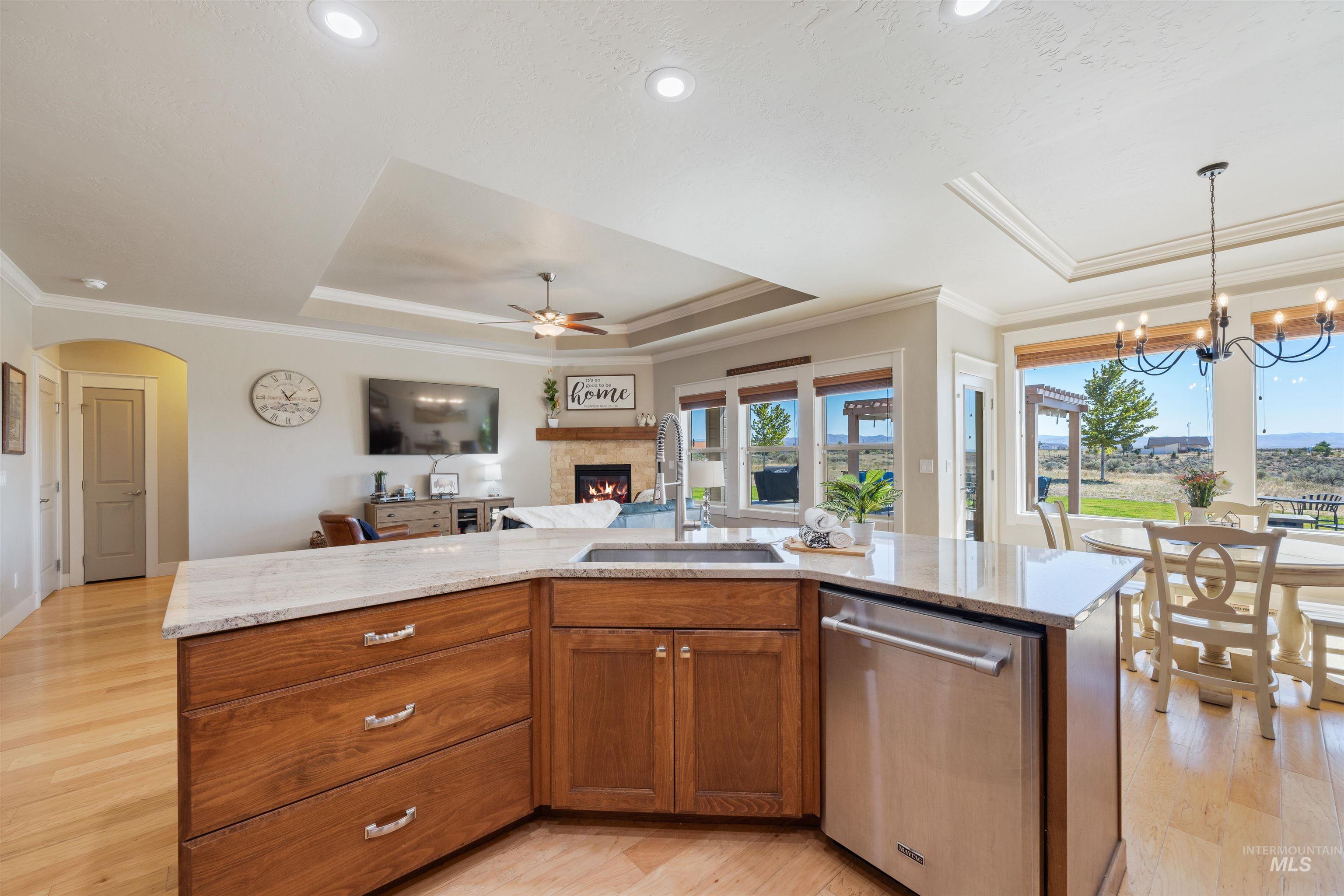 Kitchen with a raised ceiling, brown cabinets, a center island with sink, stainless steel dishwasher, and crown molding